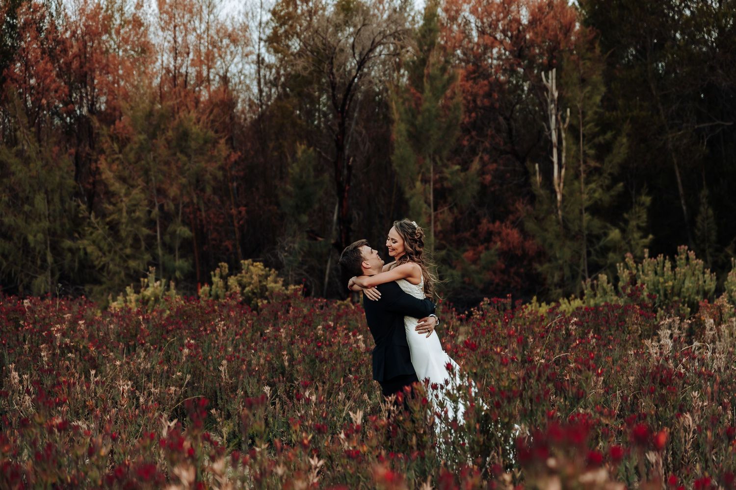 Dancing newlyweds spin joyfully in field of red wildflowers during autumn.