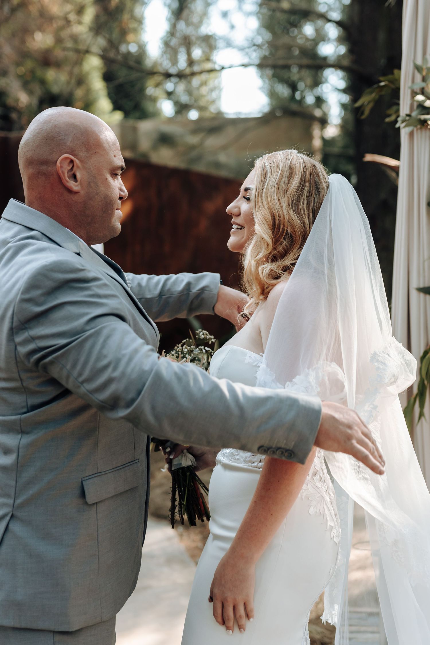 Intimate outdoor wedding moment captured between couple during veil adjustment ceremony.