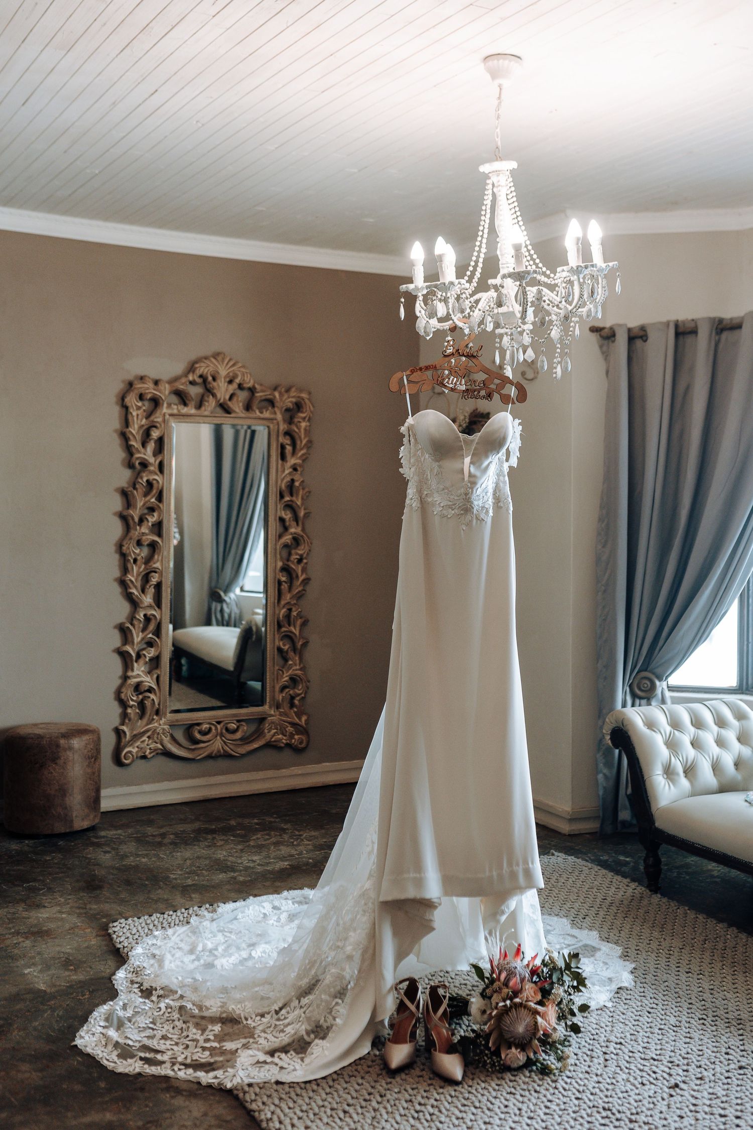Elegant white wedding dress hanging from crystal chandelier in luxurious dressing room.