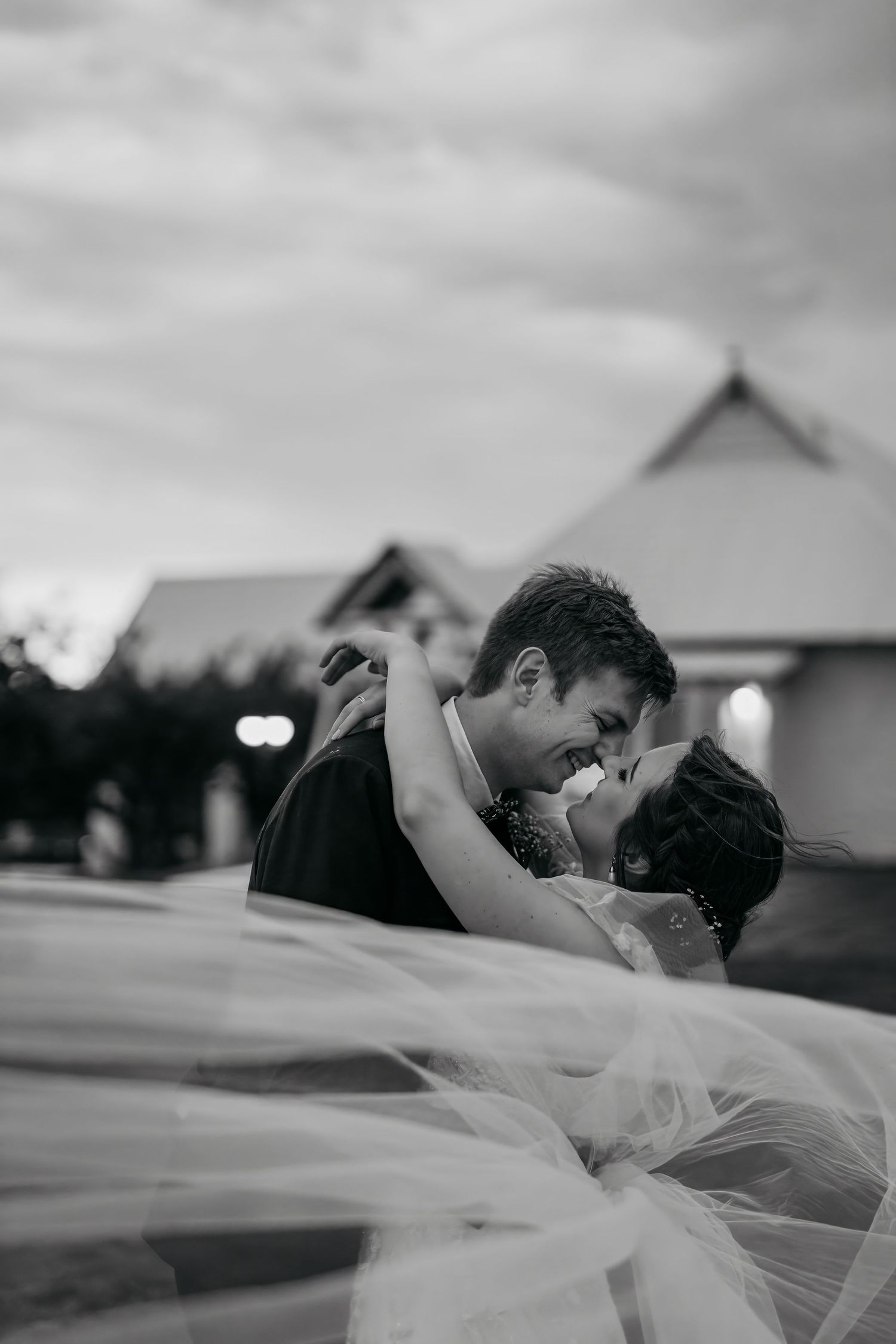 Dramatic black and white wedding photo capturing an intimate moment with flowing veil details.