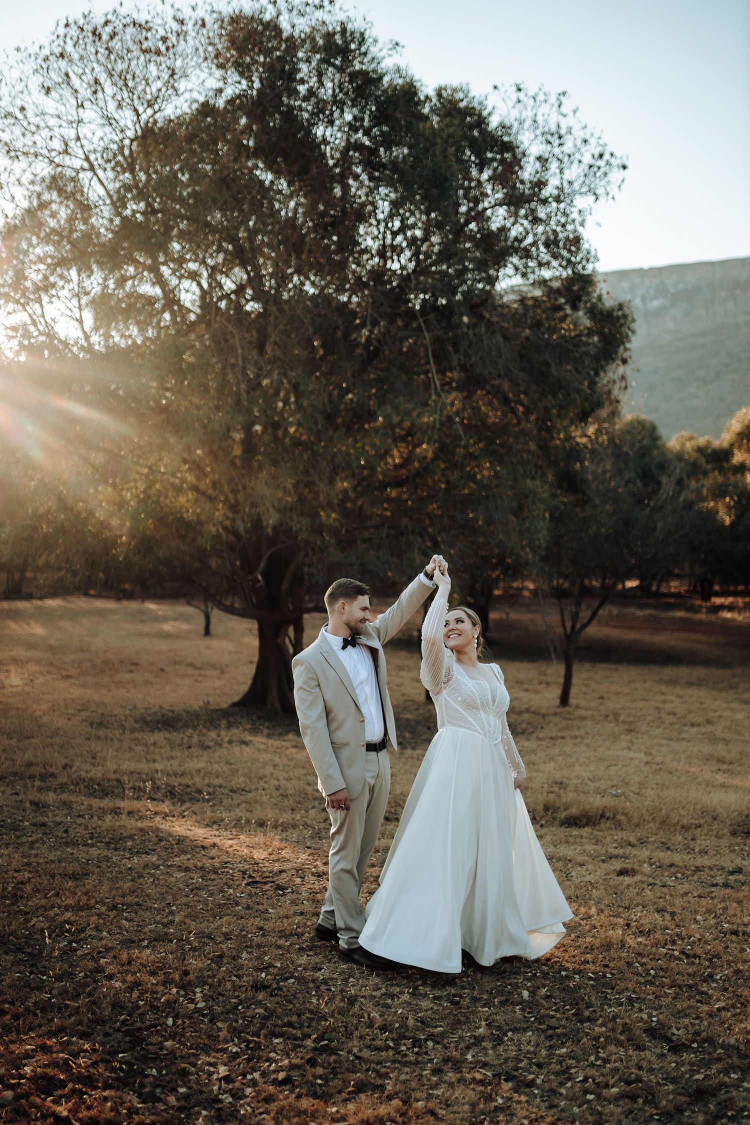 A couple shares a celebratory dance move in a sun-lit forest setting.
