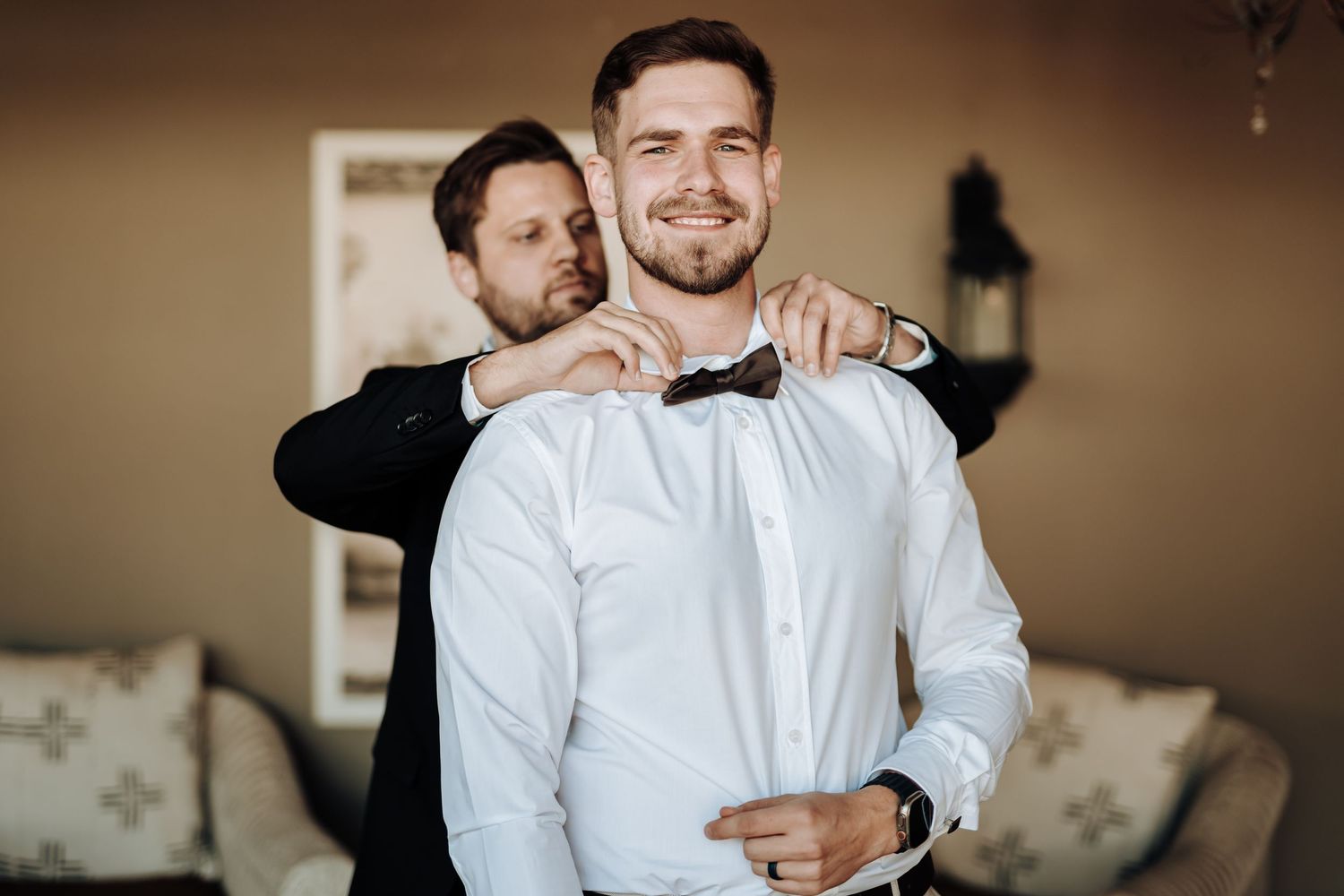 Wedding preparation scene with bow tie adjustment in an elegant interior setting.