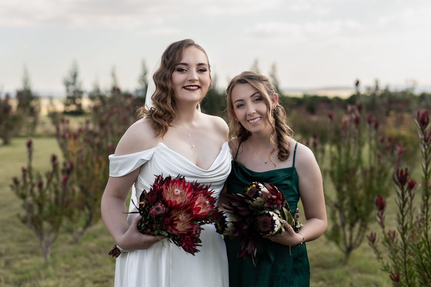 Wedding party members pose with bouquets among red flowering bushes.