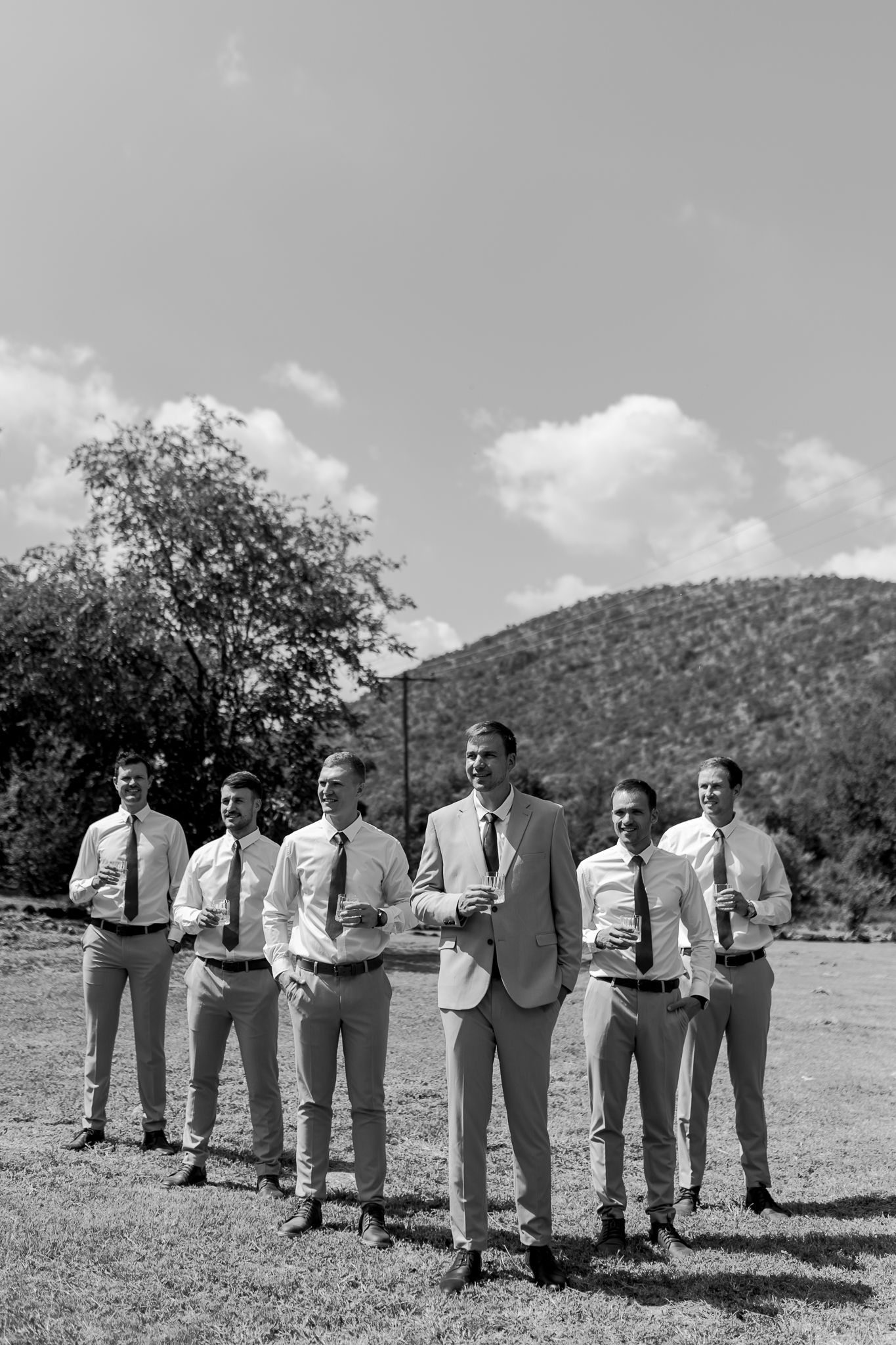Black and white photo of wedding party standing in line with mountain backdrop.