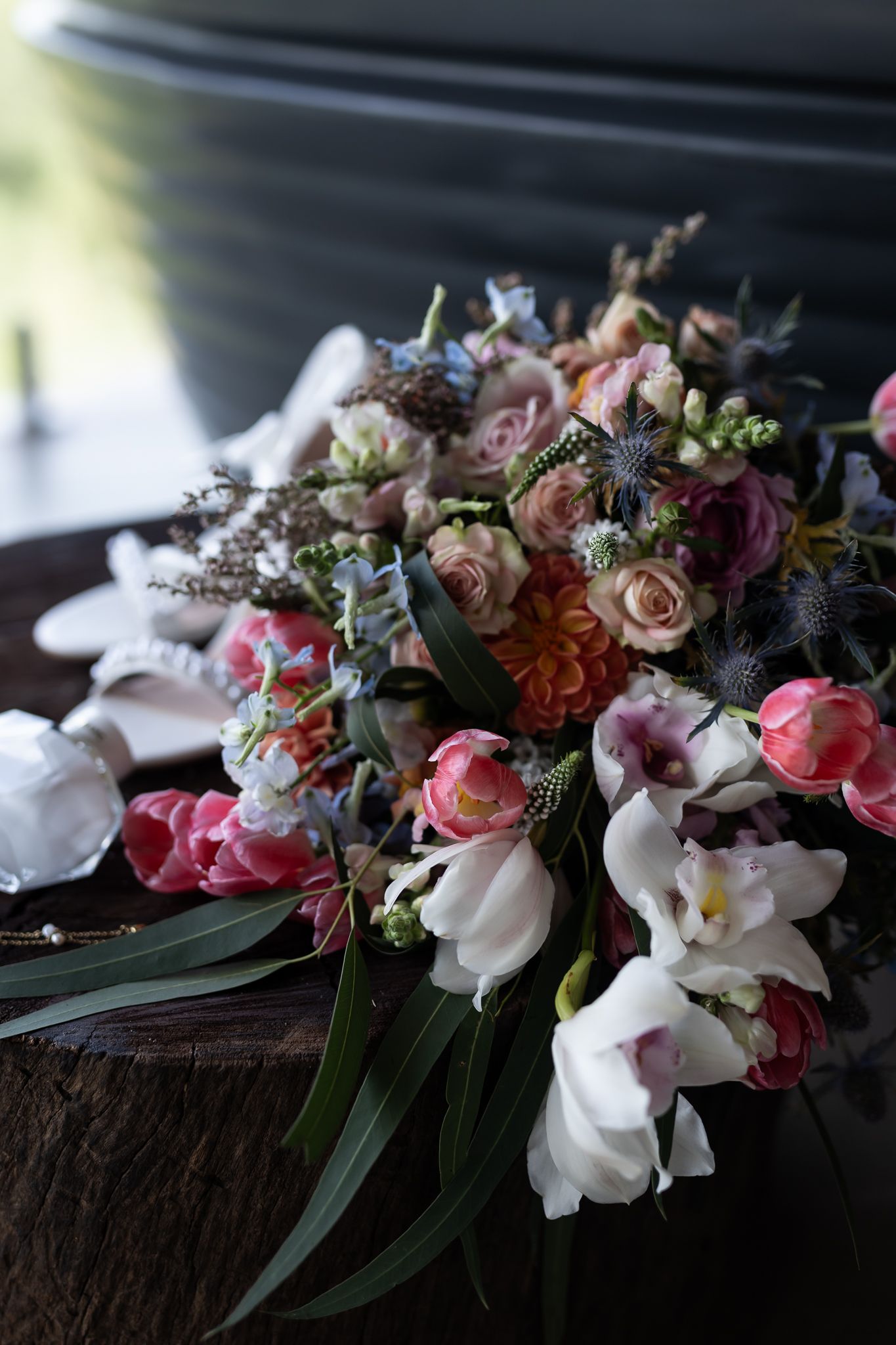 Lush wedding bouquet with pink roses, white orchids and mixed flowers in moody lighting.