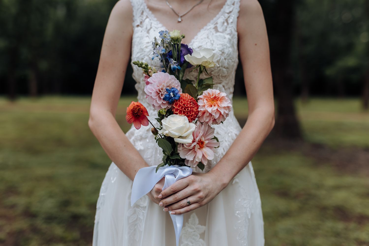 Colorful wedding bouquet with red, pink and purple flowers against white lace dress.