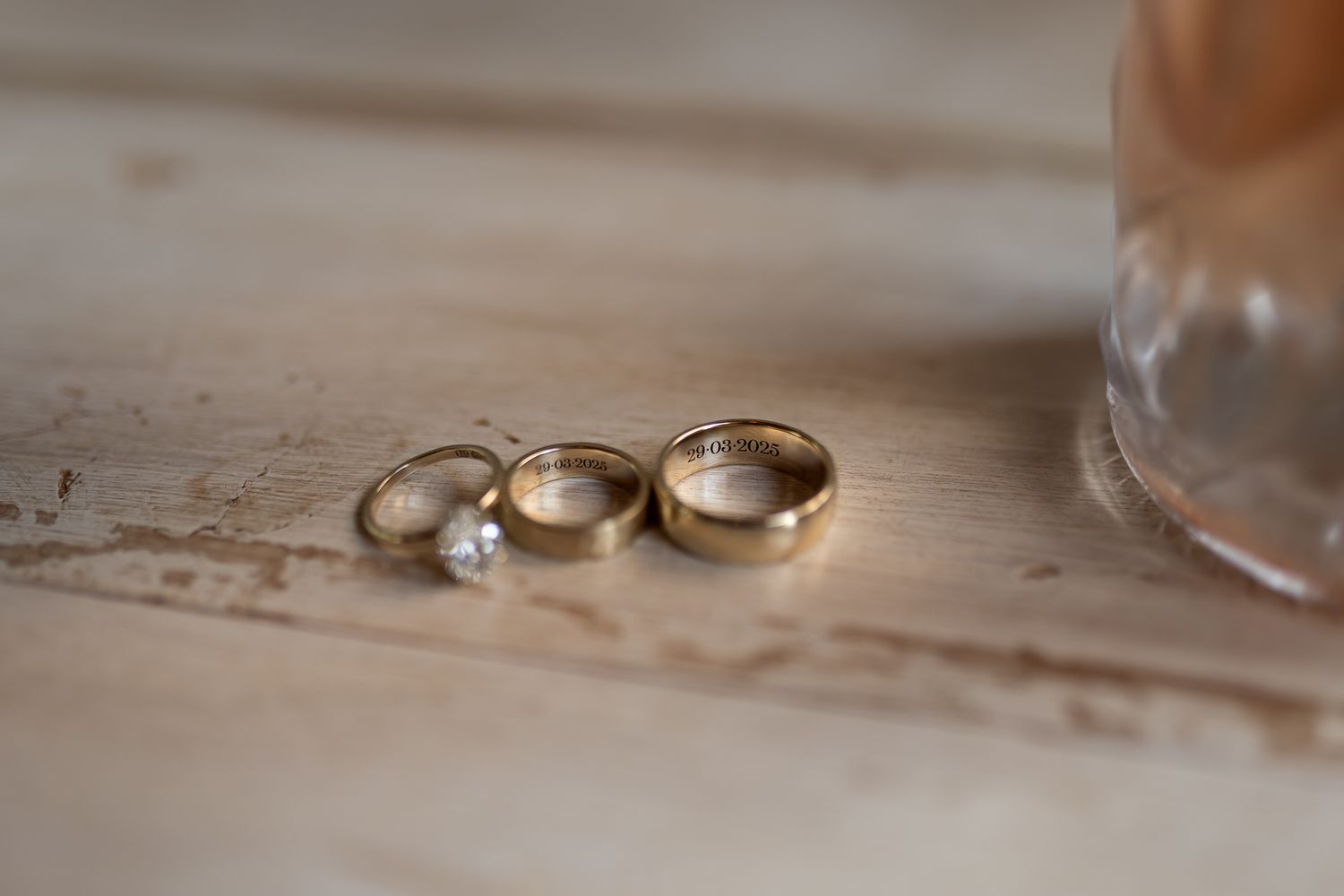 Wedding rings and engagement ring arranged on rustic wooden surface in natural light.