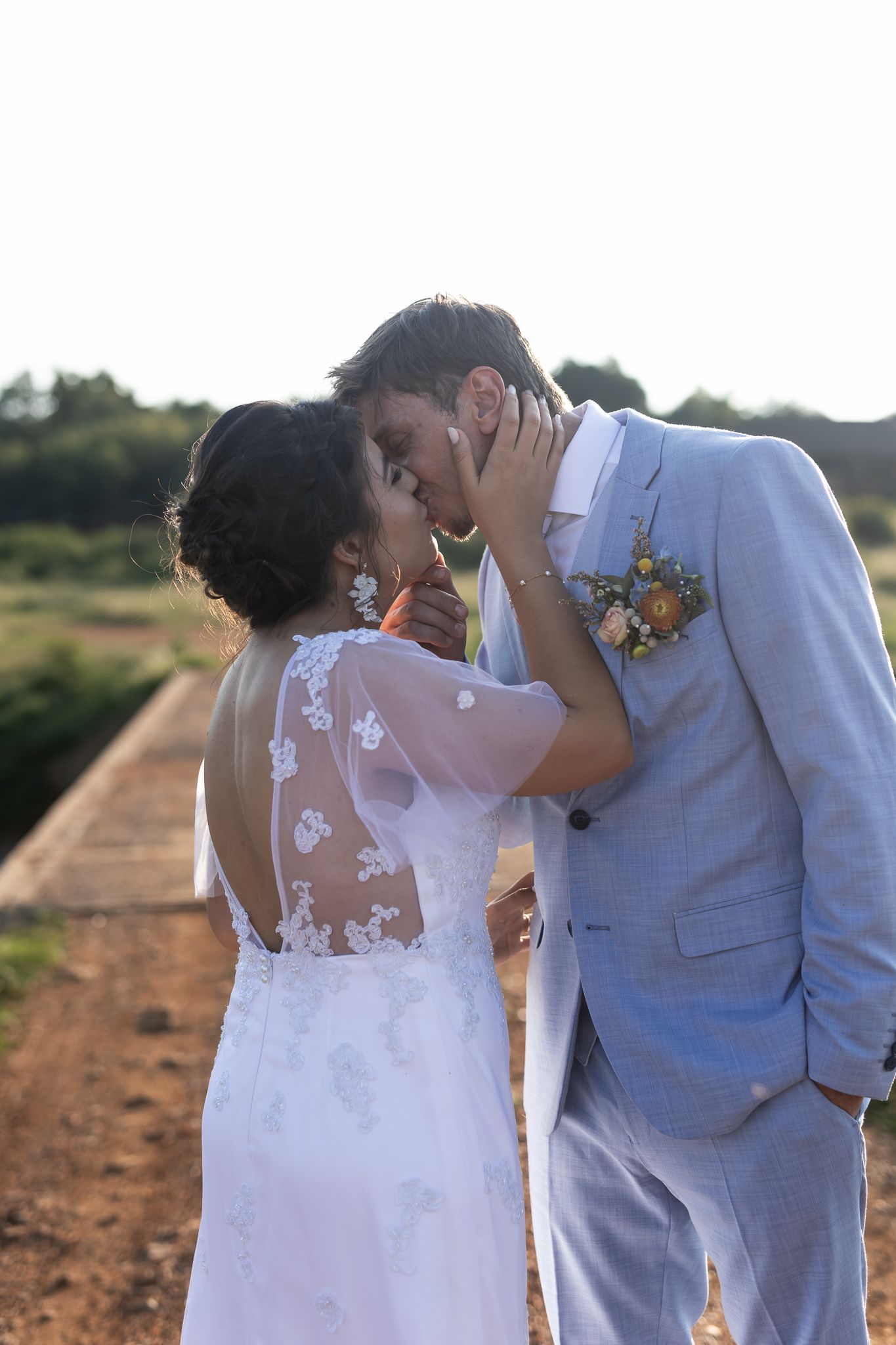 Intimate wedding moment captured on a dirt path with water in background.