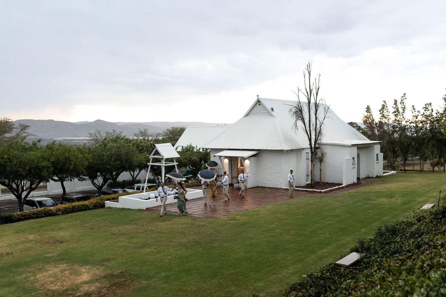 White wedding venue building with lawn and mountains in the background on an overcast day.