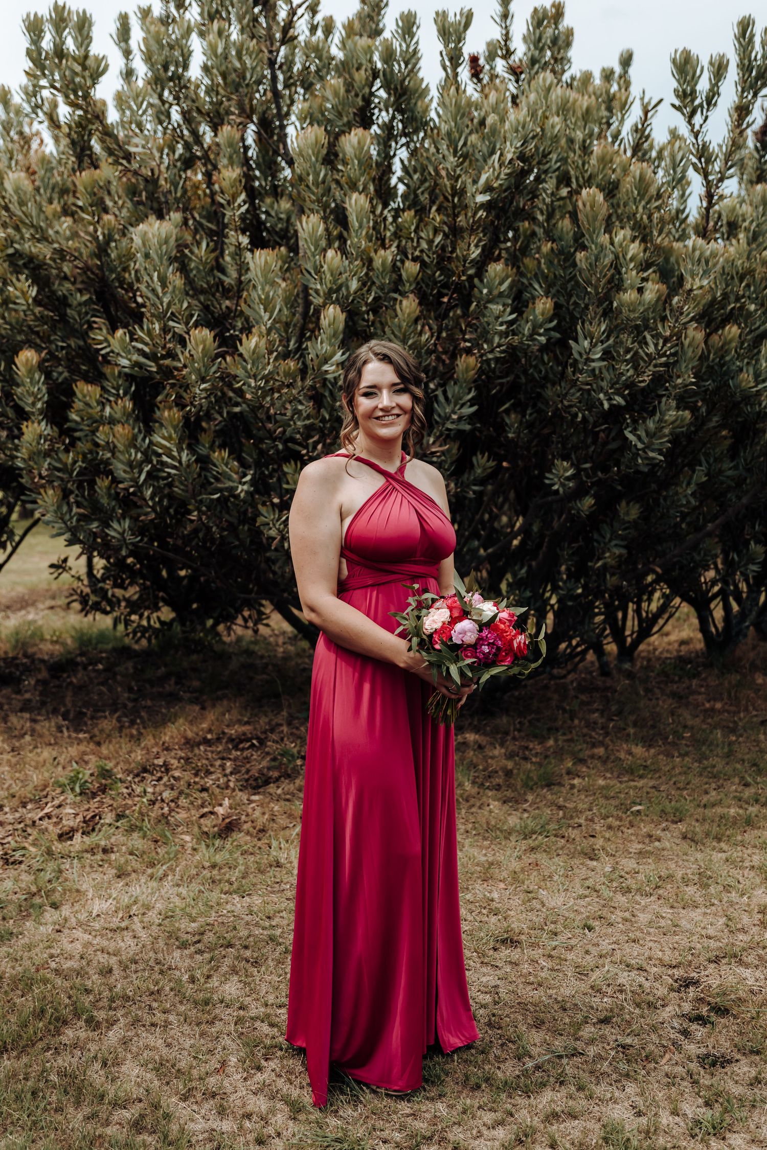 Full length portrait of bridesmaid in red halter dress holding pink and red bouquet.