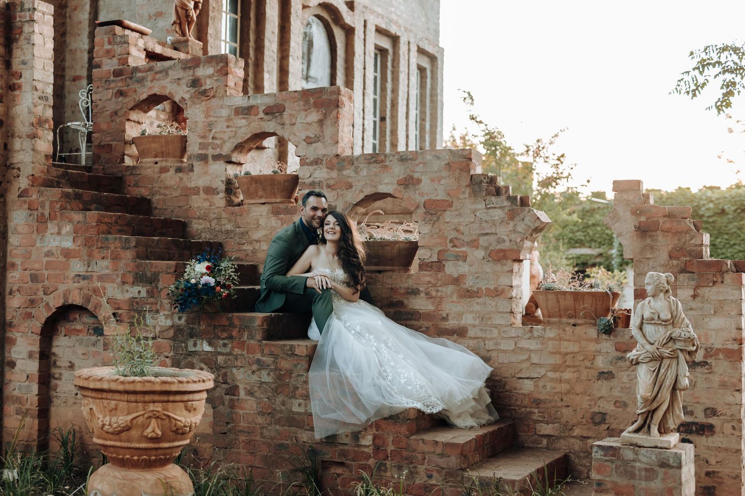 Wedding photography on antique brick steps with classical statues and terracotta planters.
