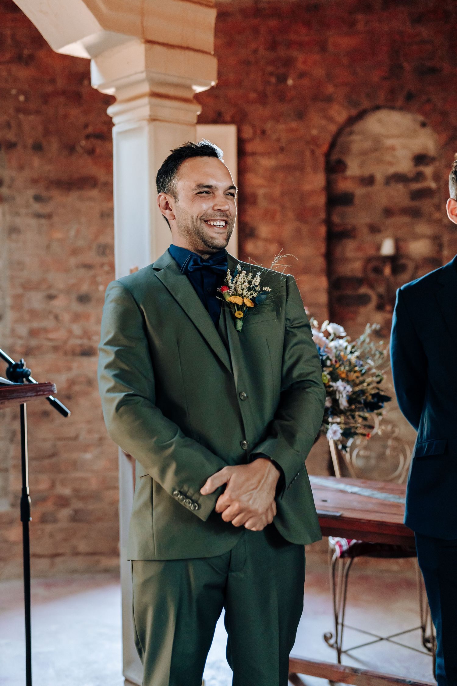 Person in green suit laughing during wedding ceremony in brick venue.