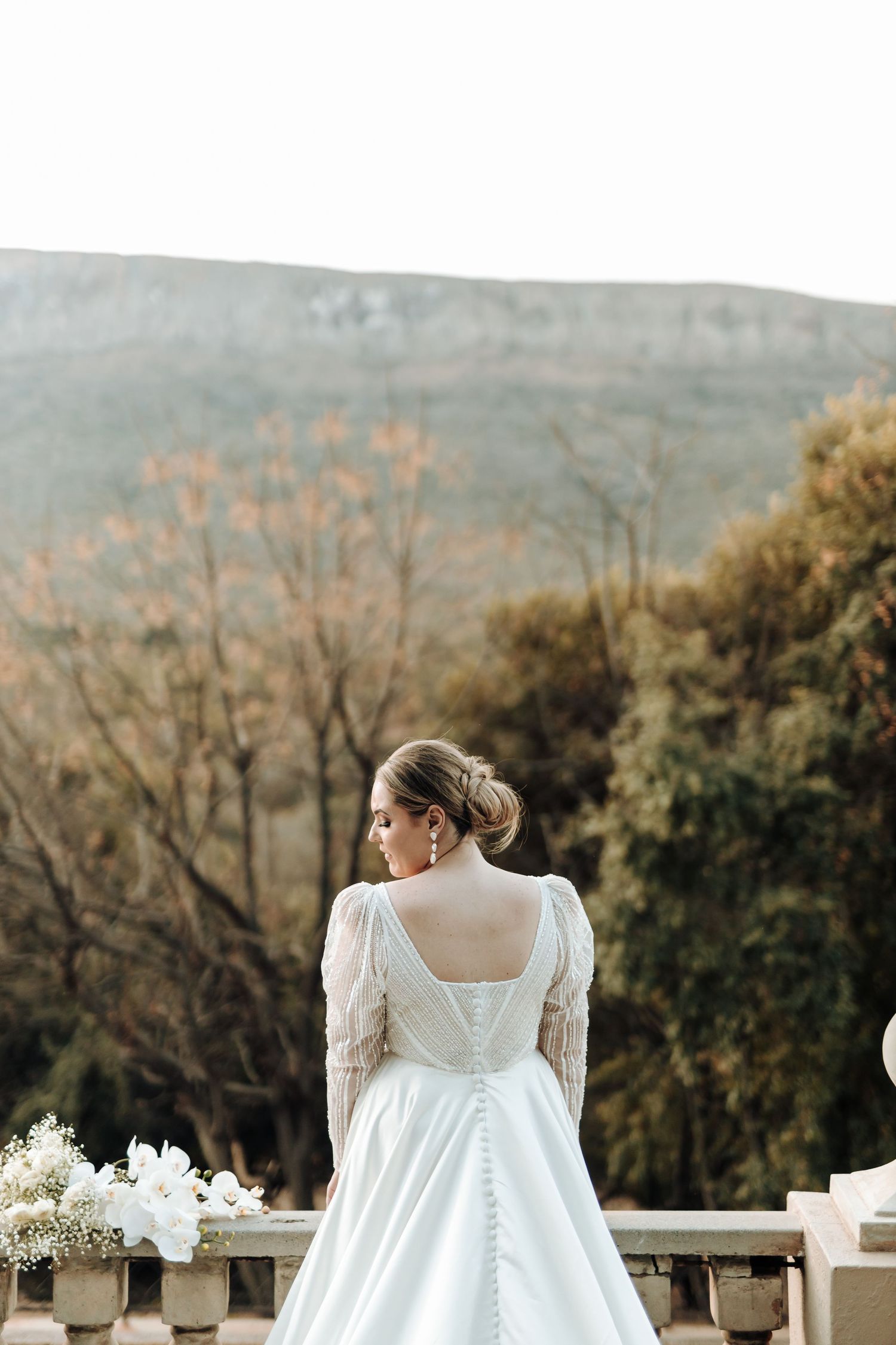 Classic white wedding dress with button detail overlooking mountain landscape.