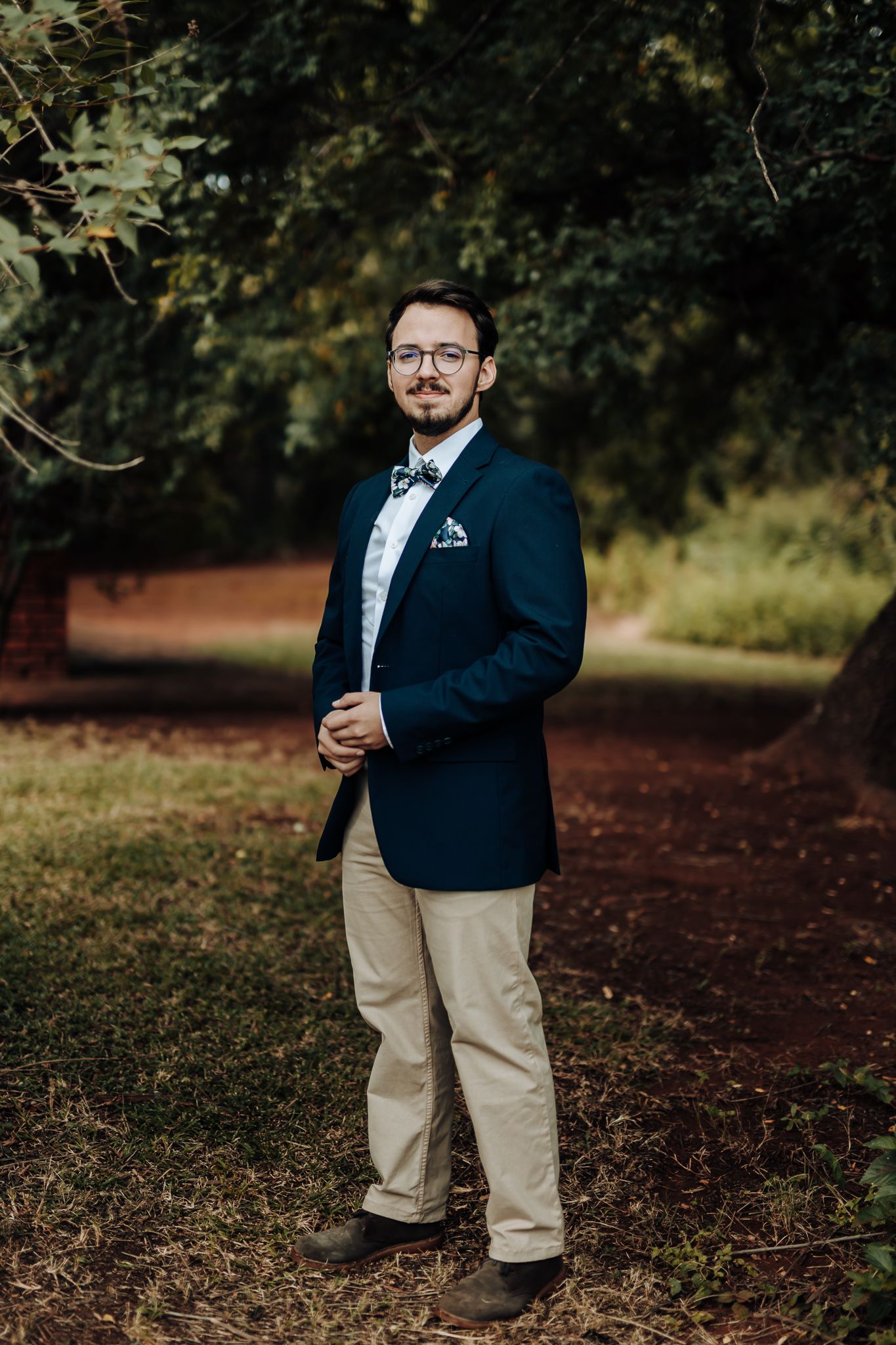 Full length portrait of groom in navy blazer and khakis standing in garden setting.