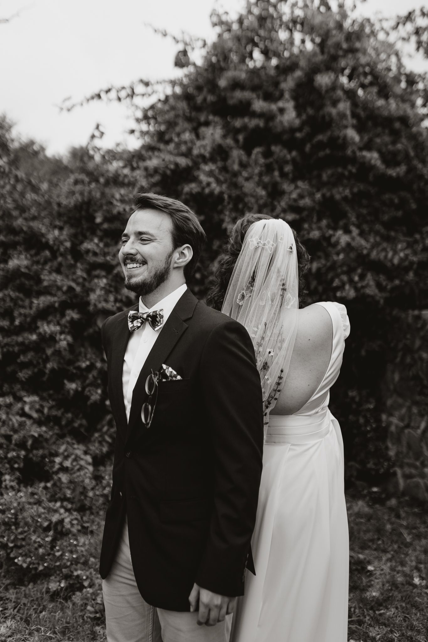 Black and white portrait of wedding couple doing a first look pose in a garden setting.