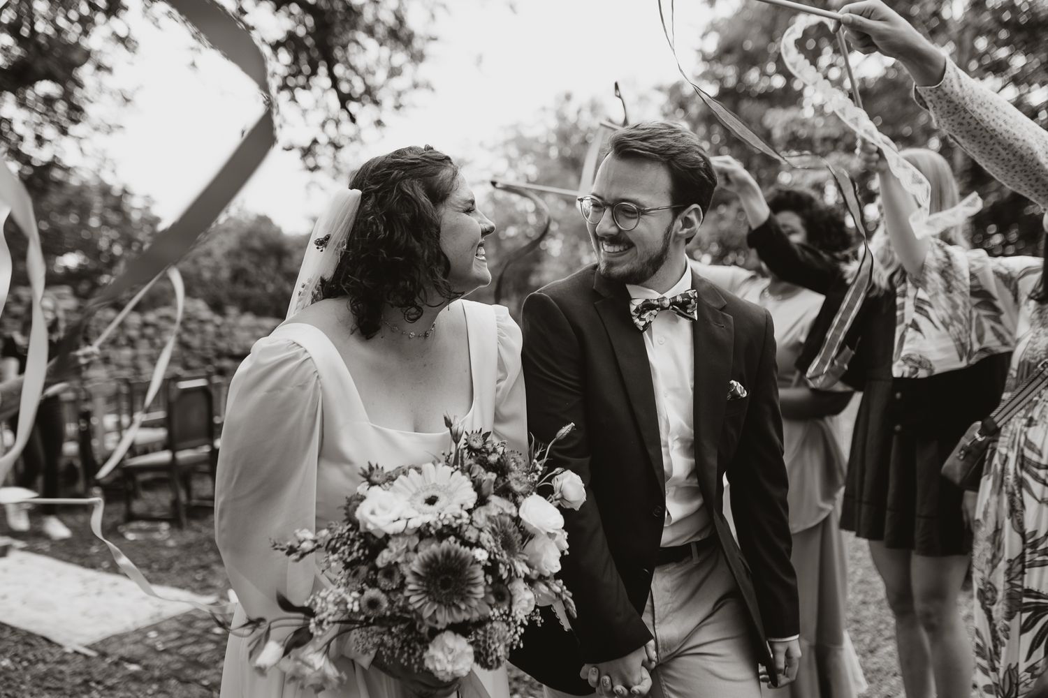 A black and white photo of newlyweds celebrating with guests at their outdoor wedding.