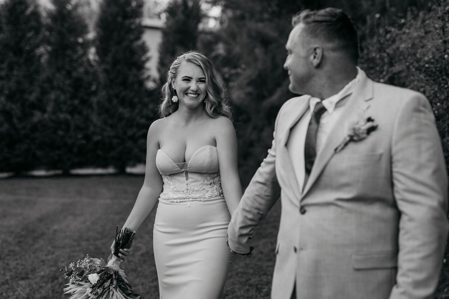 Wedding couple sharing joyful moment outdoors with evergreen trees in background.