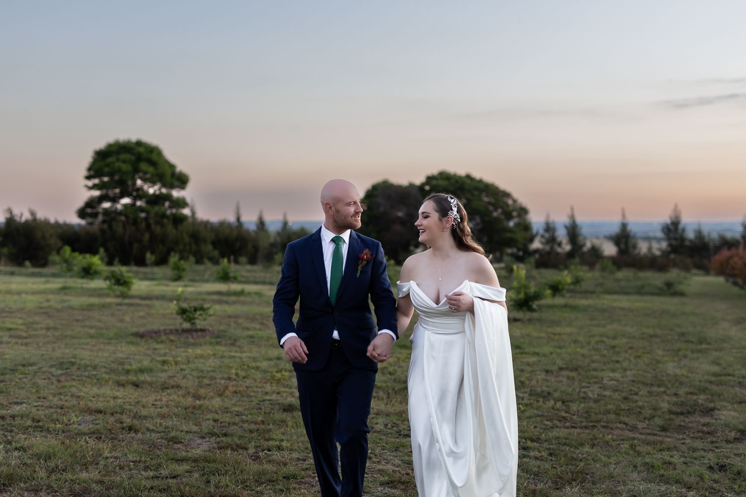 A romantic sunset wedding portrait captured in a scenic field with trees in the background.