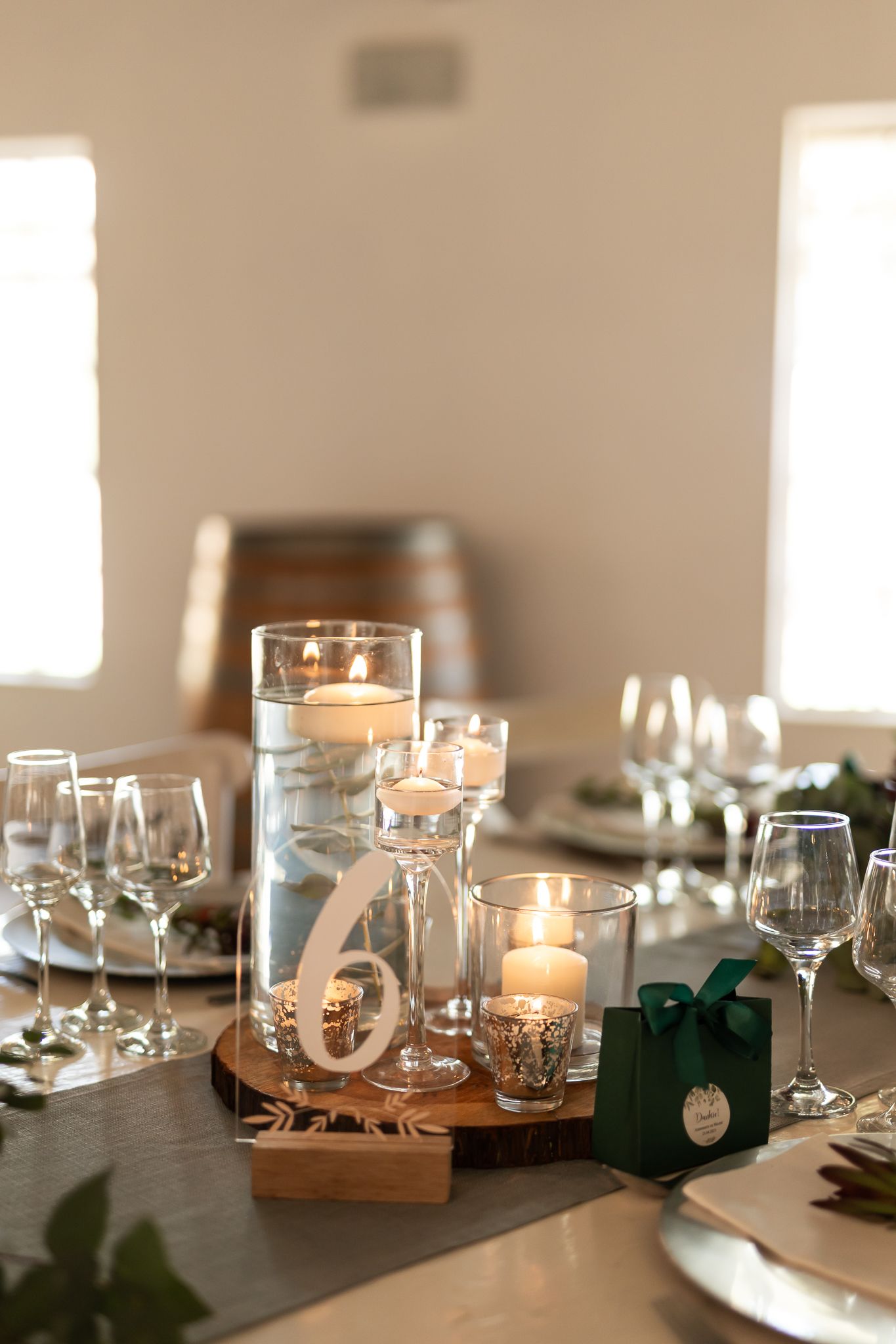 Wedding table decor with floating candles, table number six, and wine glasses on dark surface.