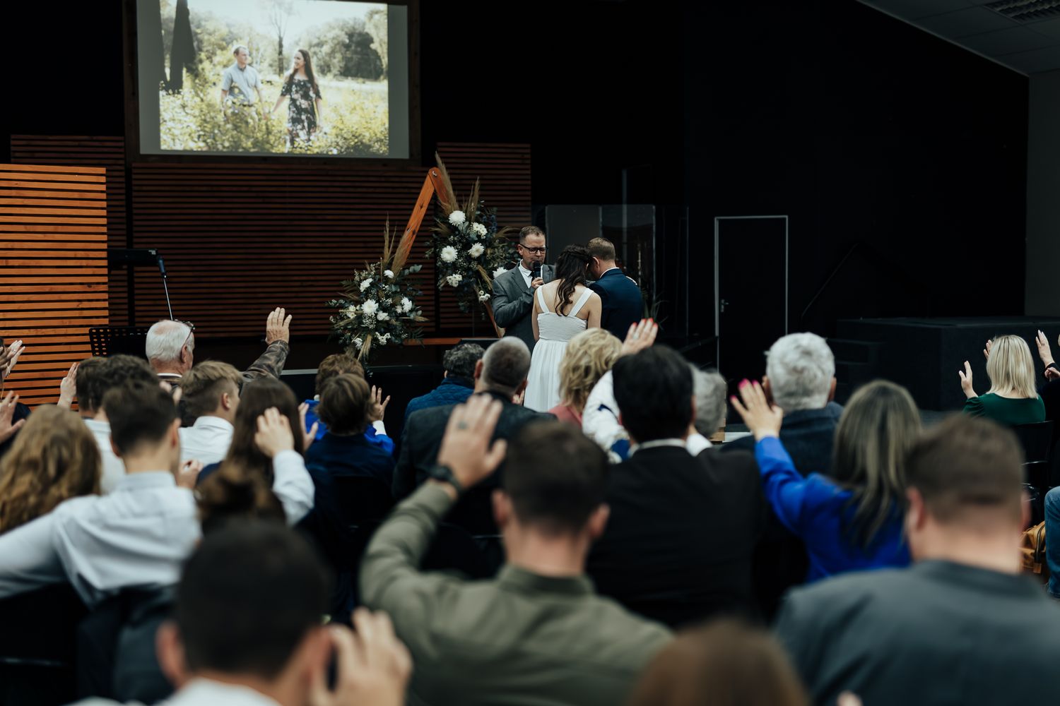 A crowd of wedding guests raising their hands during a church ceremony.