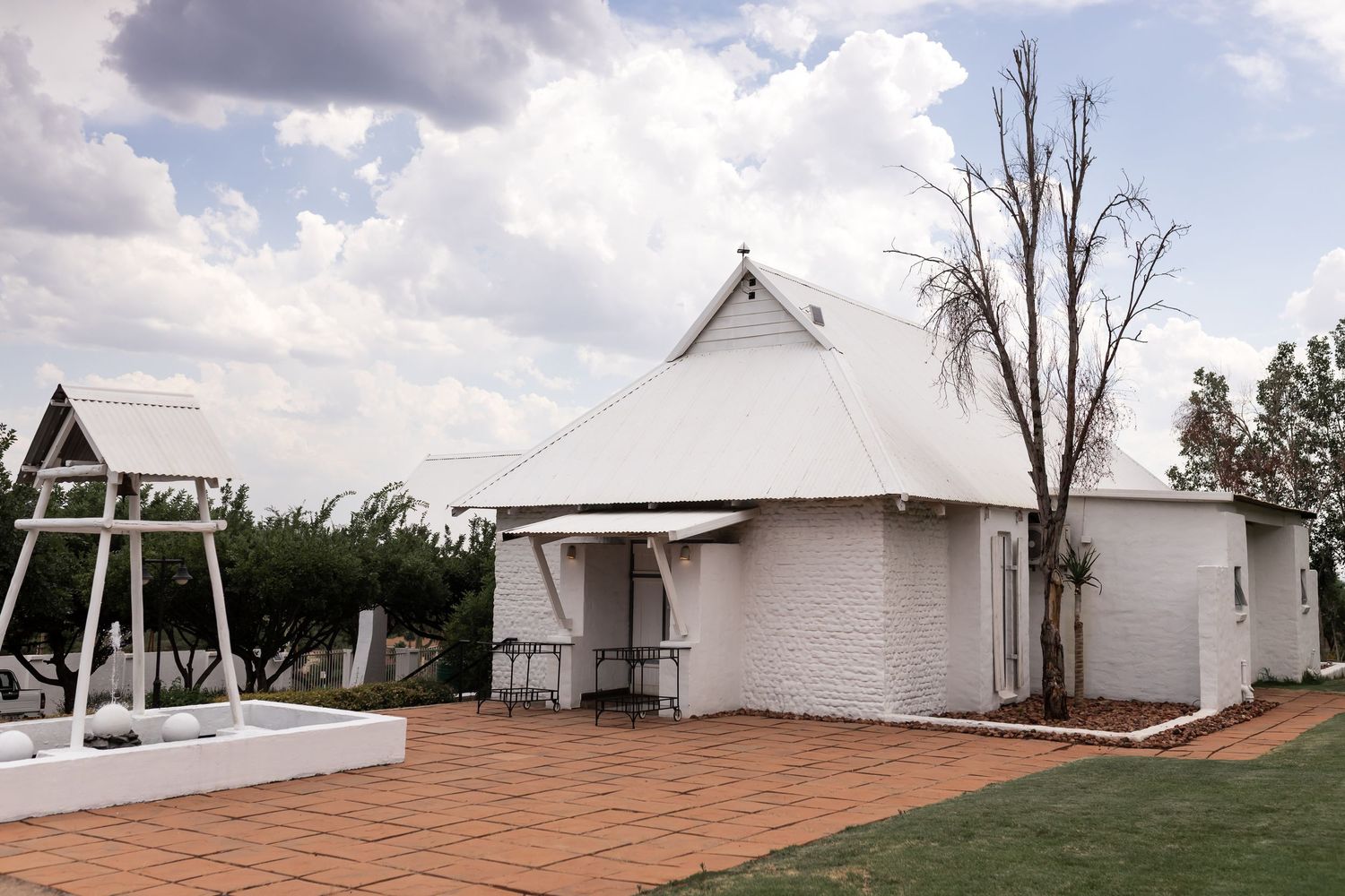 White chapel building with wooden deck and play structure in surrounding garden setting.