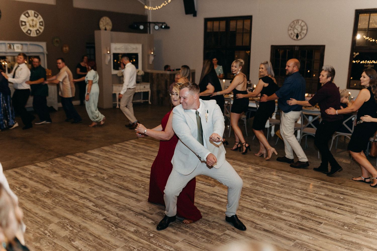 Wedding guests showing off dance moves on wooden floor during reception celebration.