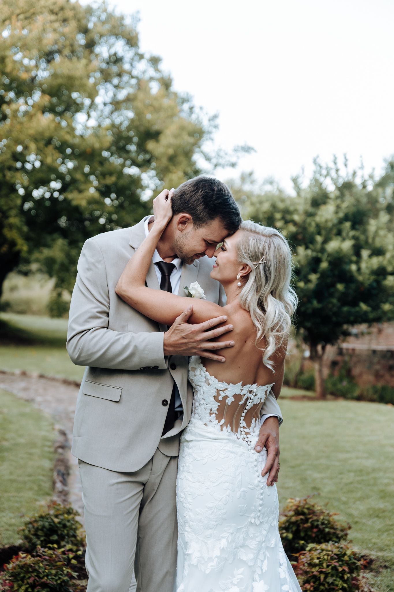 Romantic outdoor portrait of couple in elegant wedding attire embracing on grassy lawn.