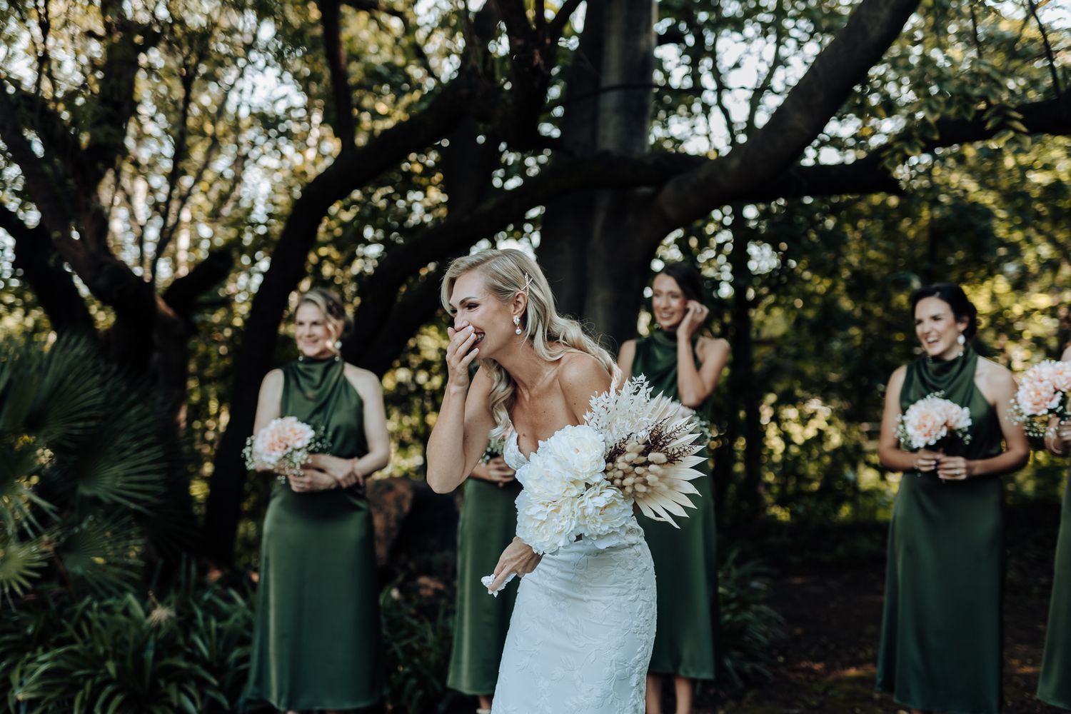 Wedding scene with emerald-dressed attendants watching someone in white hold a dramatic floral bouquet.