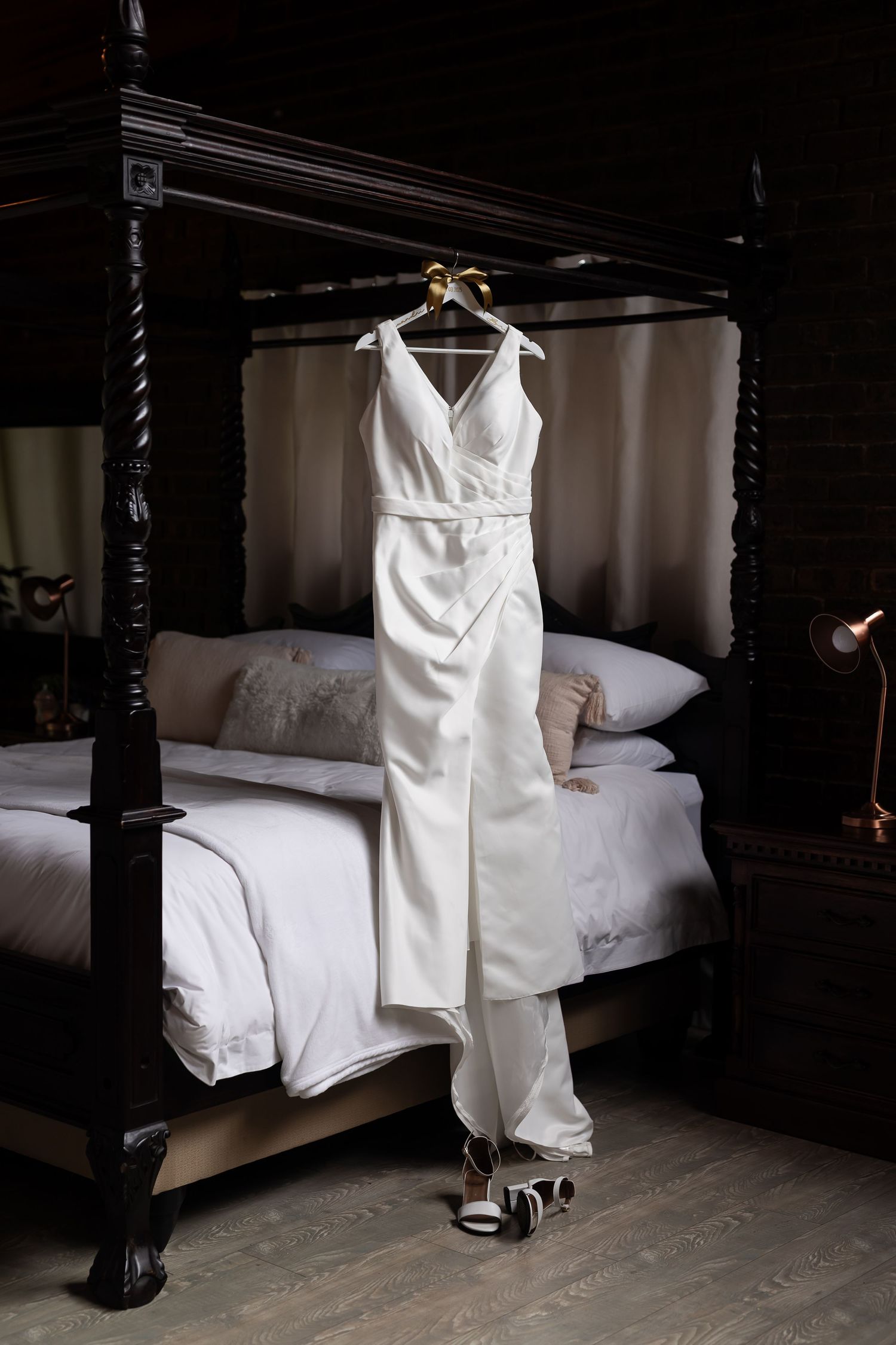 Elegant white wedding dress hanging on a four-poster bed with vintage dark wood frame.