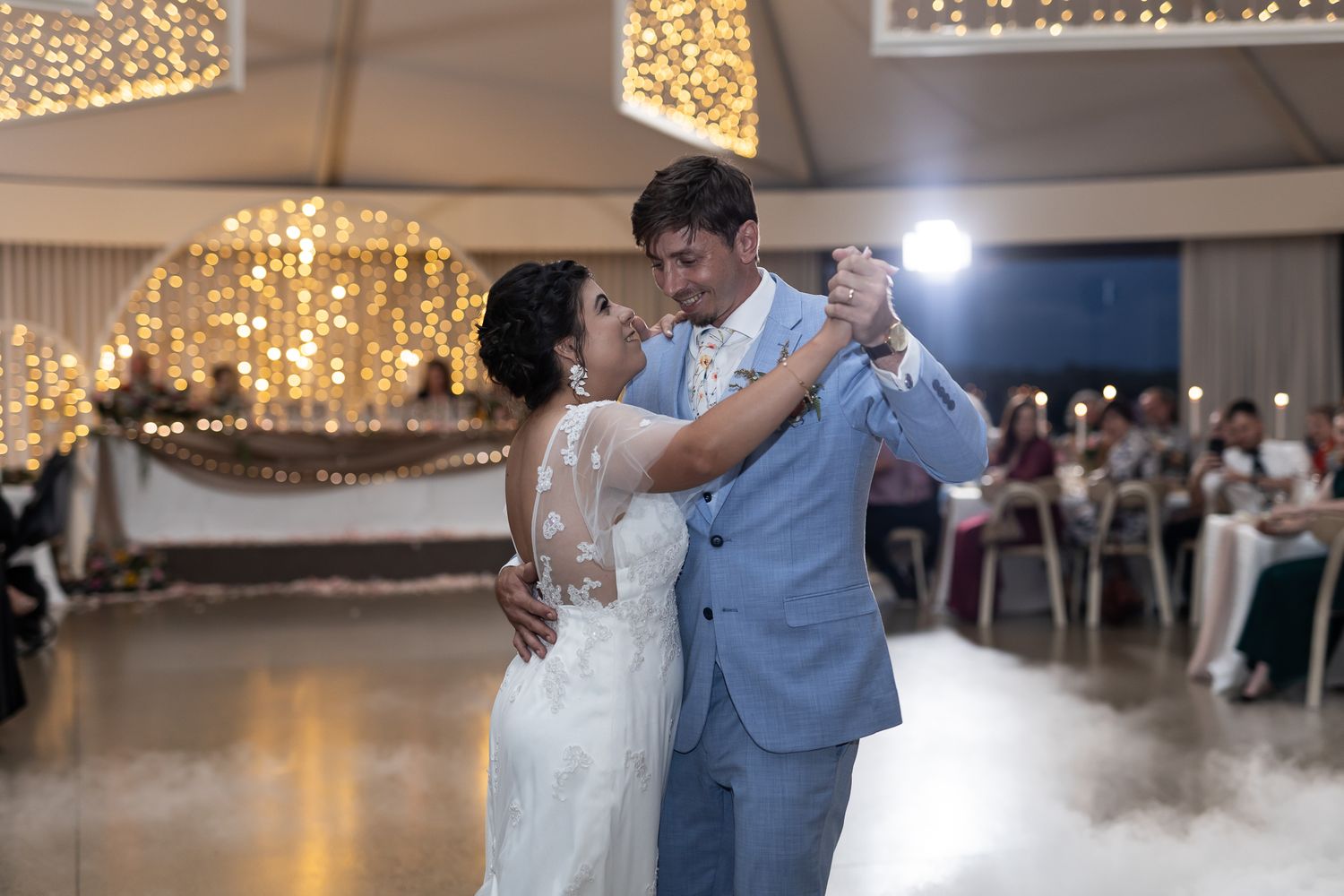 A couple performs an intimate slow dance in a light-filled reception hall with guests watching.