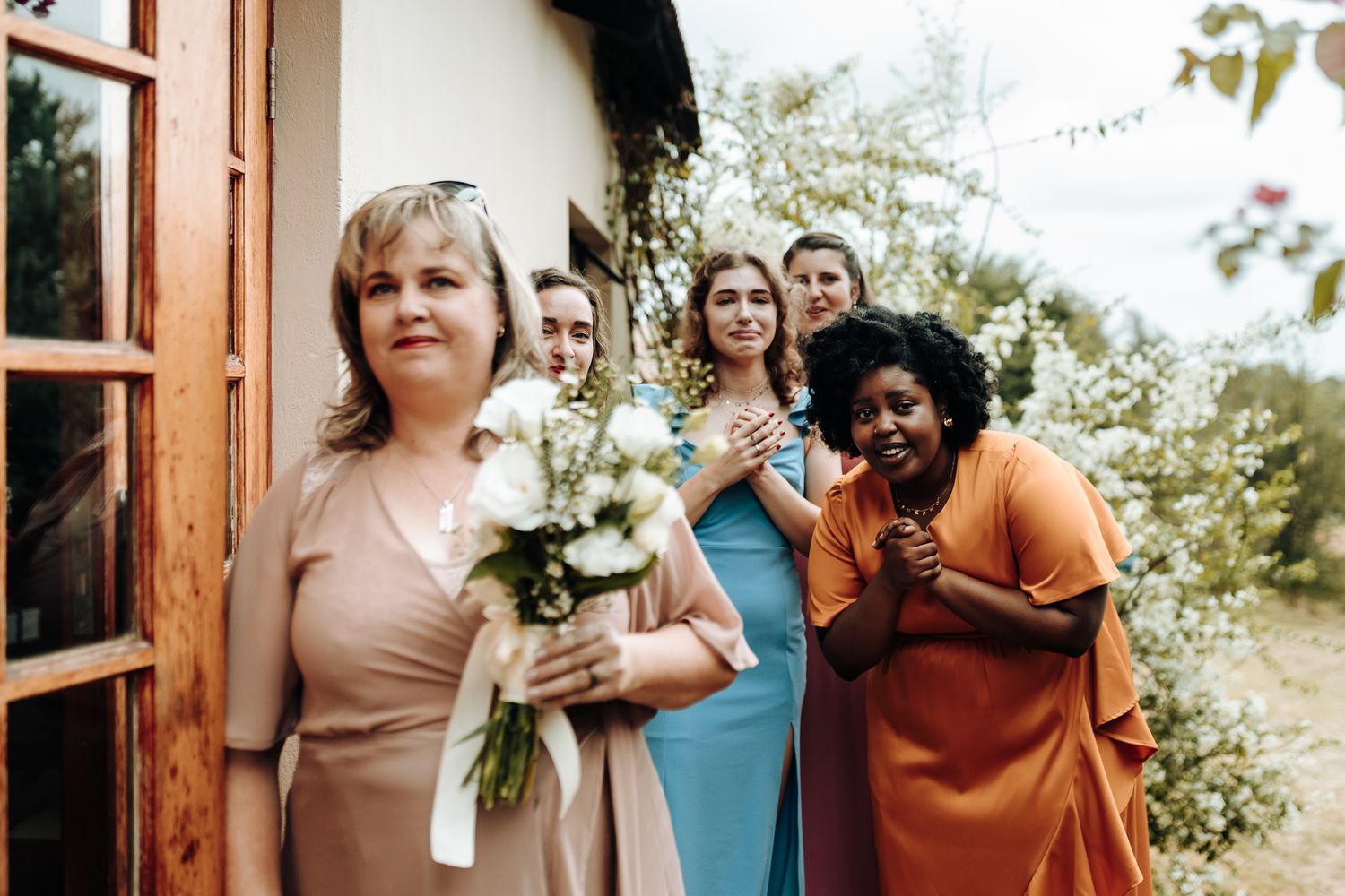 Wedding party members in colorful dresses sharing a joyful moment outdoors.