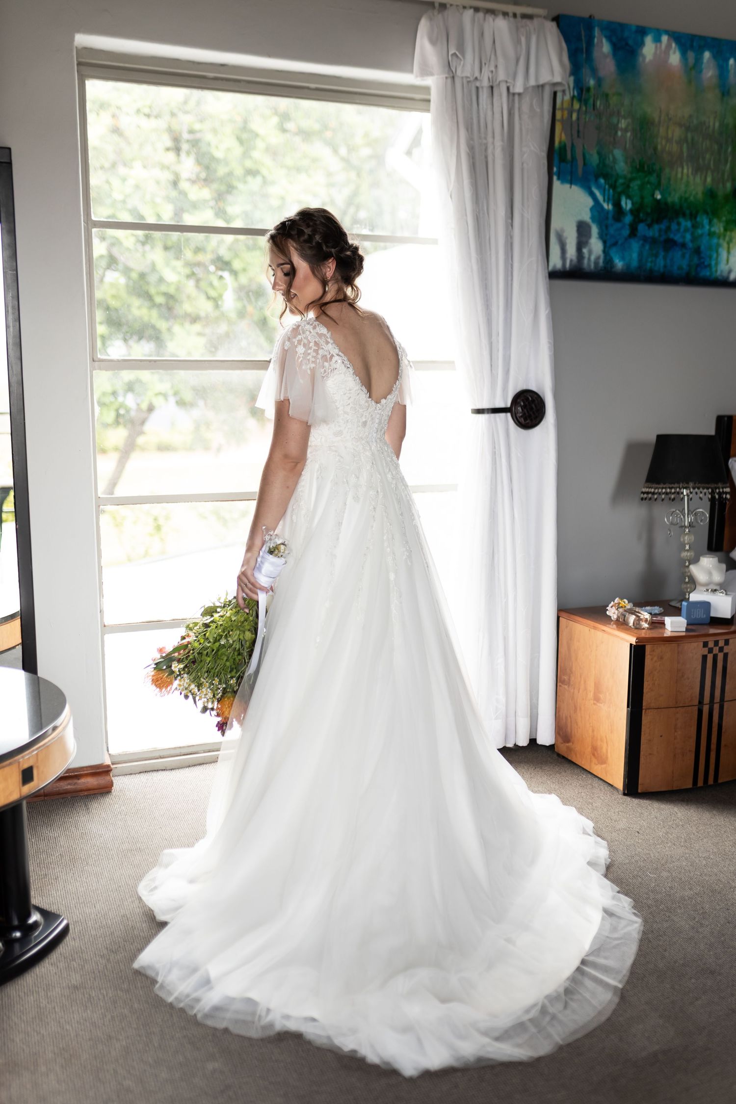 A back view of a bride in a flowing white wedding gown with lace details and sheer sleeves.