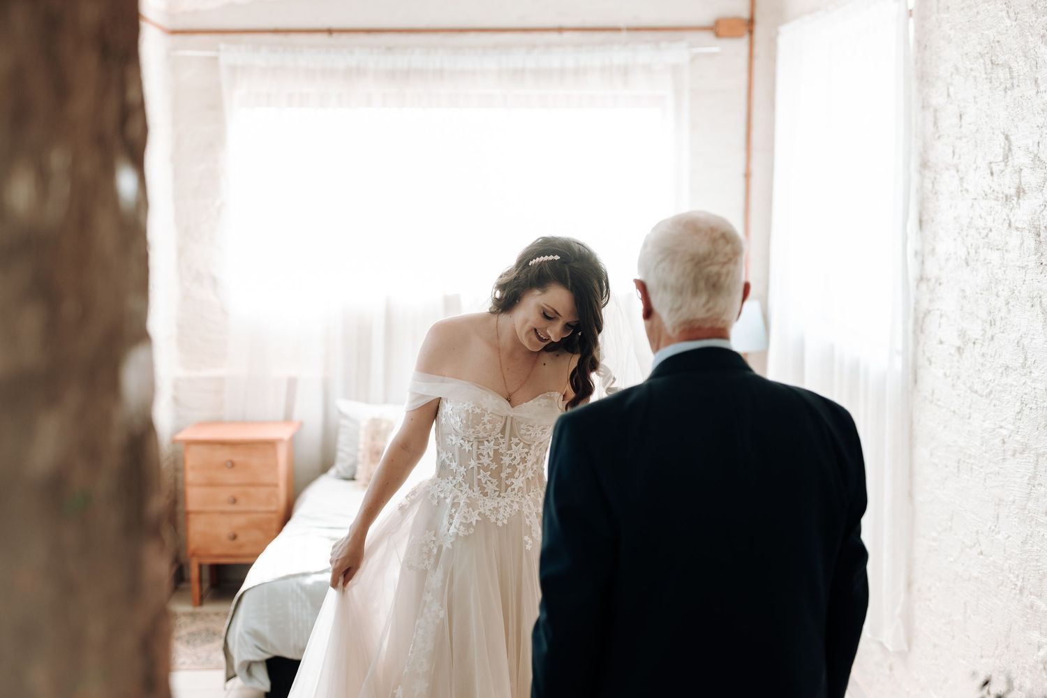 Intimate moment captured in soft lighting with wedding dress details visible.