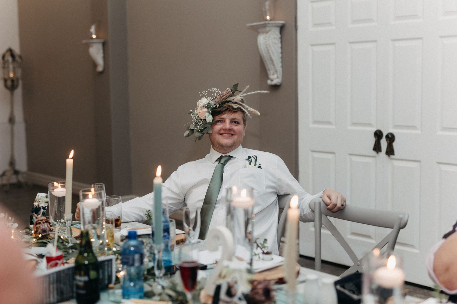 Wedding guests share laughter around an elegantly set dinner table with candles and decorative elements.