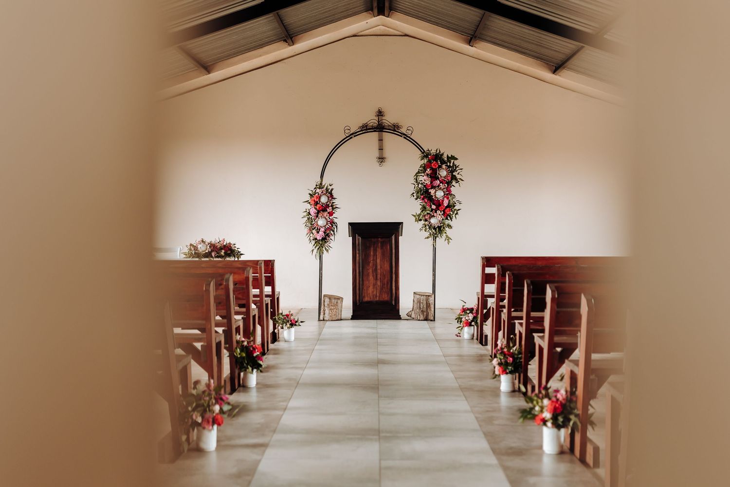 Wedding chapel aisle decorated with floral arrangements leading to an ornate metal arch.