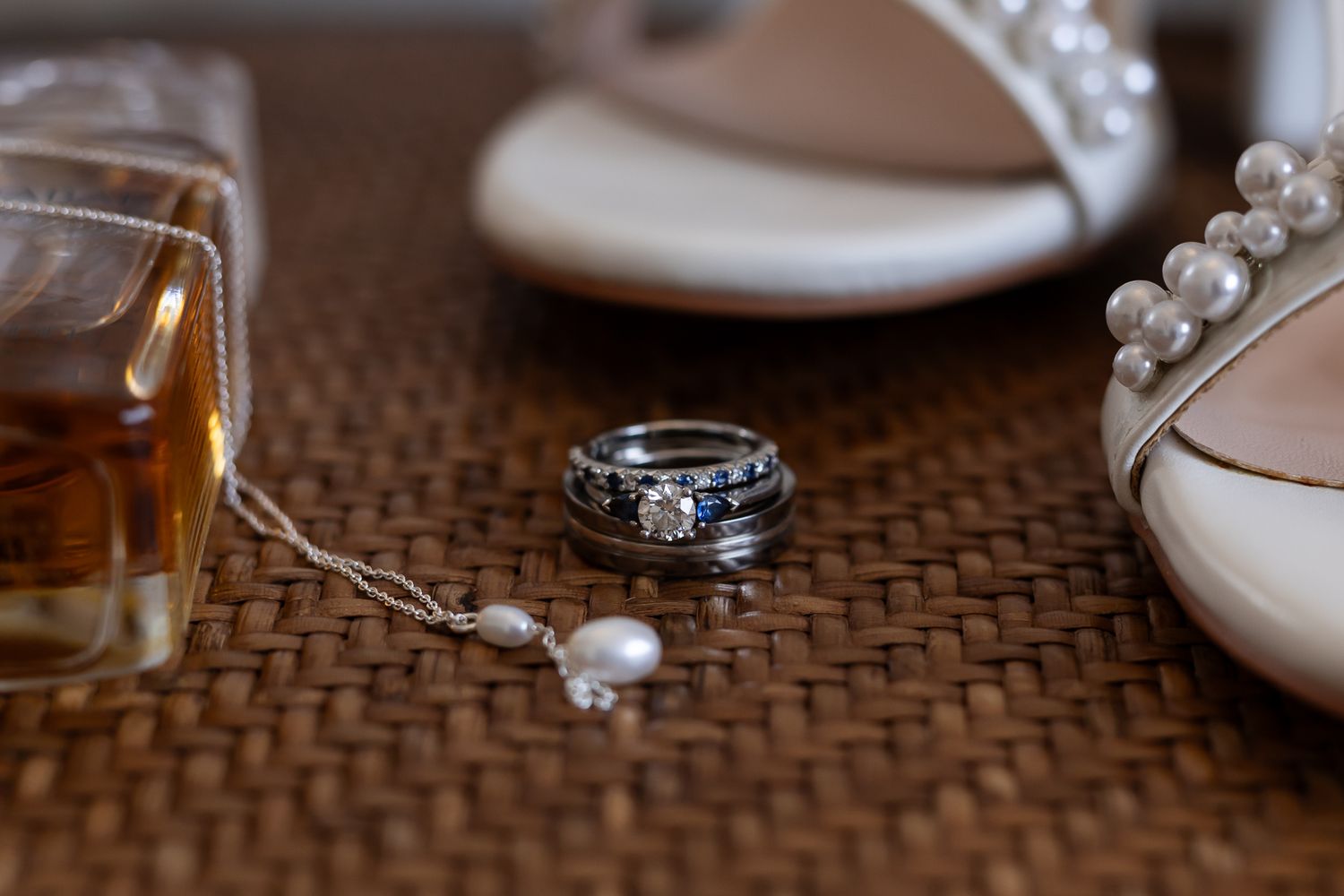 Wedding details including rings, pearls, and white shoes arranged on a textured surface.