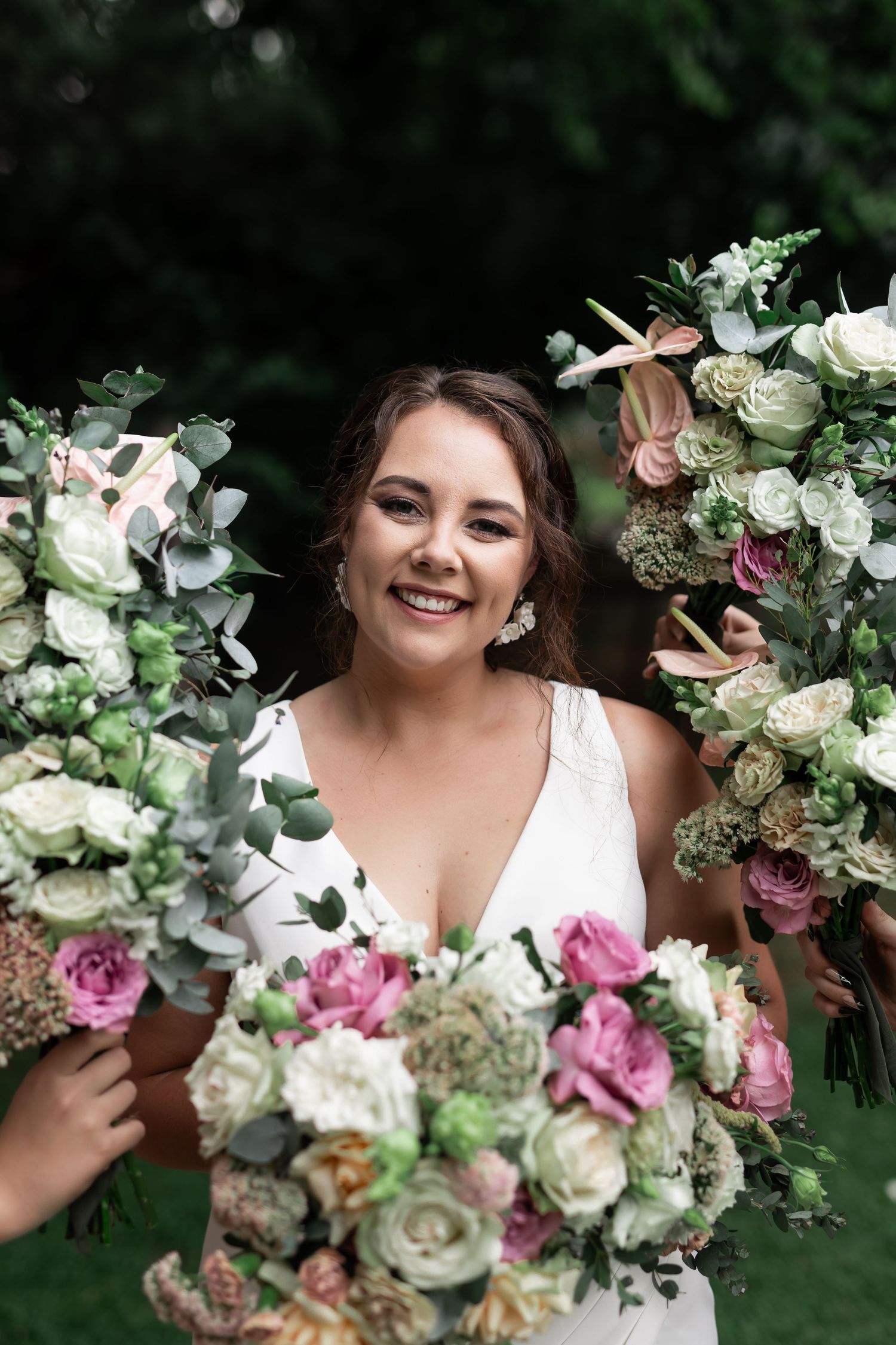 Radiant bride smiling while holding beautiful bouquets of roses and mixed flowers.
