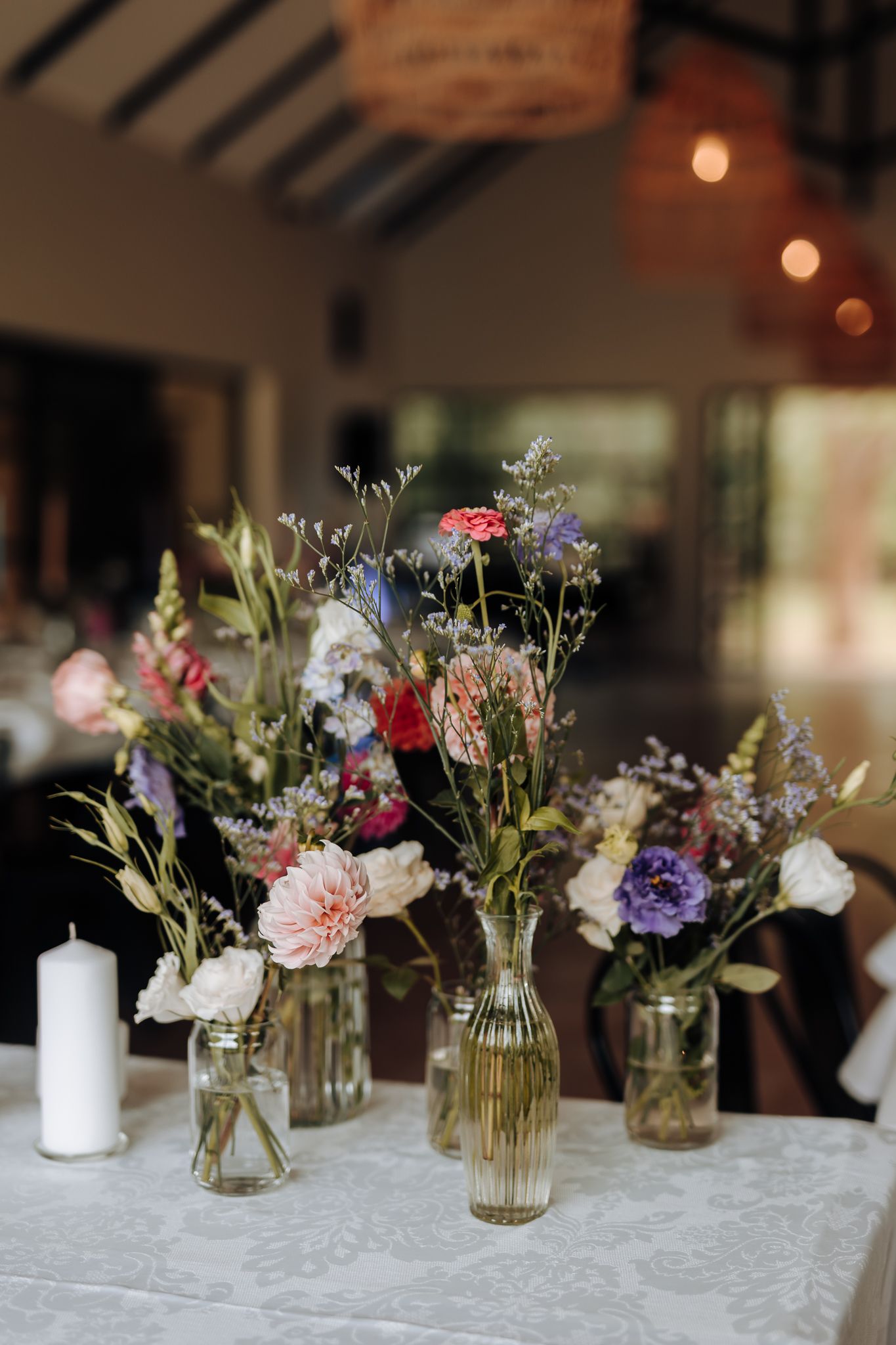 Delicate floral centerpieces in glass vases featuring pink, purple, and white wildflowers on a light tablecloth.
