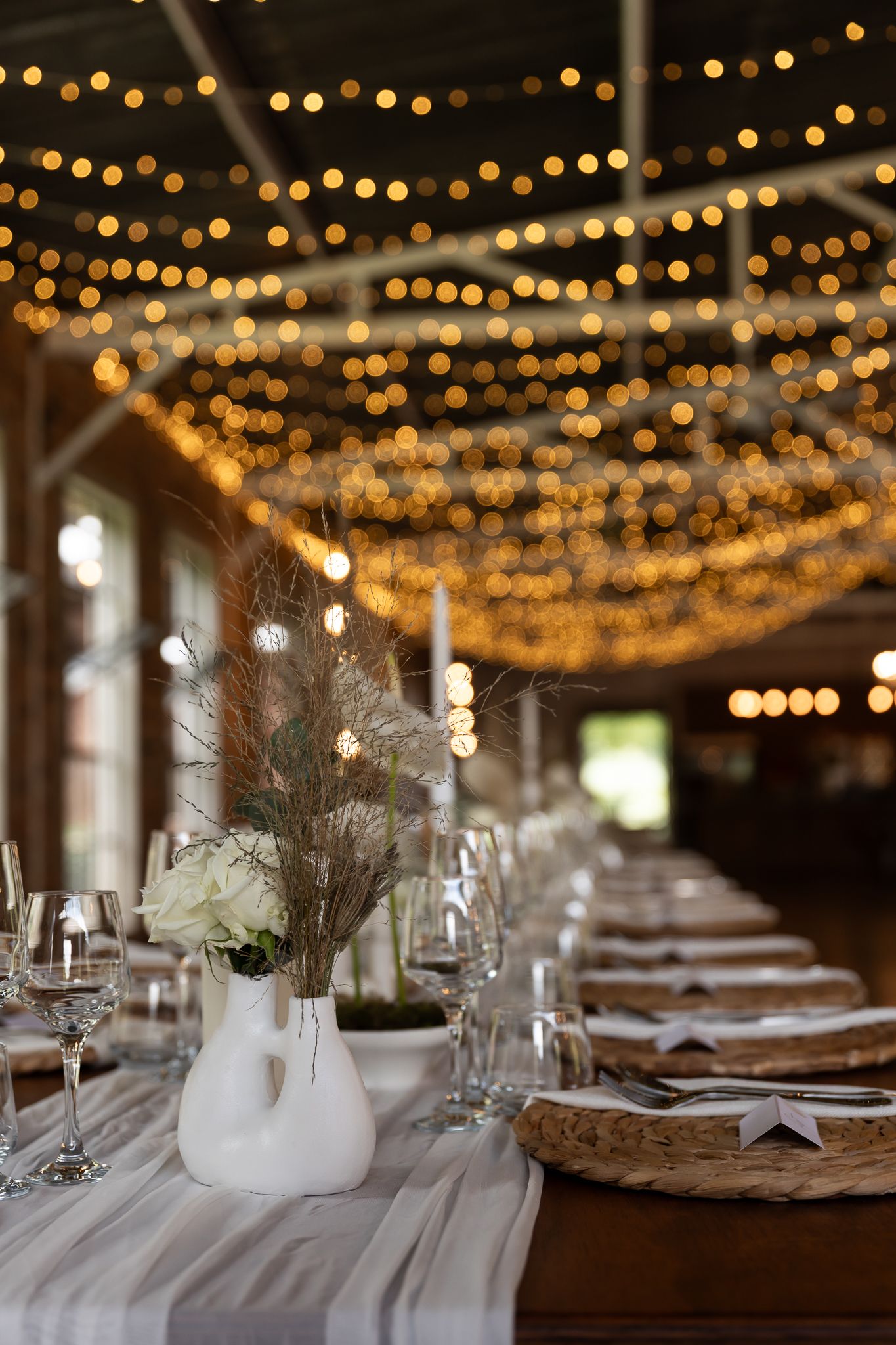 Elegant wedding reception table with fairy lights overhead and white floral centerpieces.