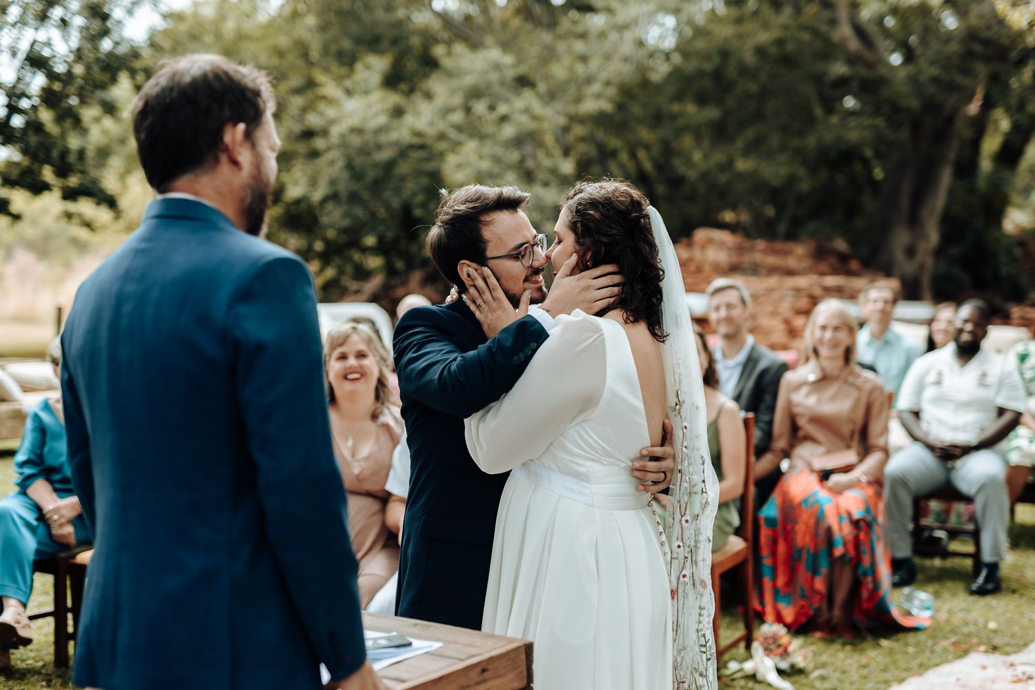 A celebratory moment during an outdoor wedding ceremony with guests watching in the background.