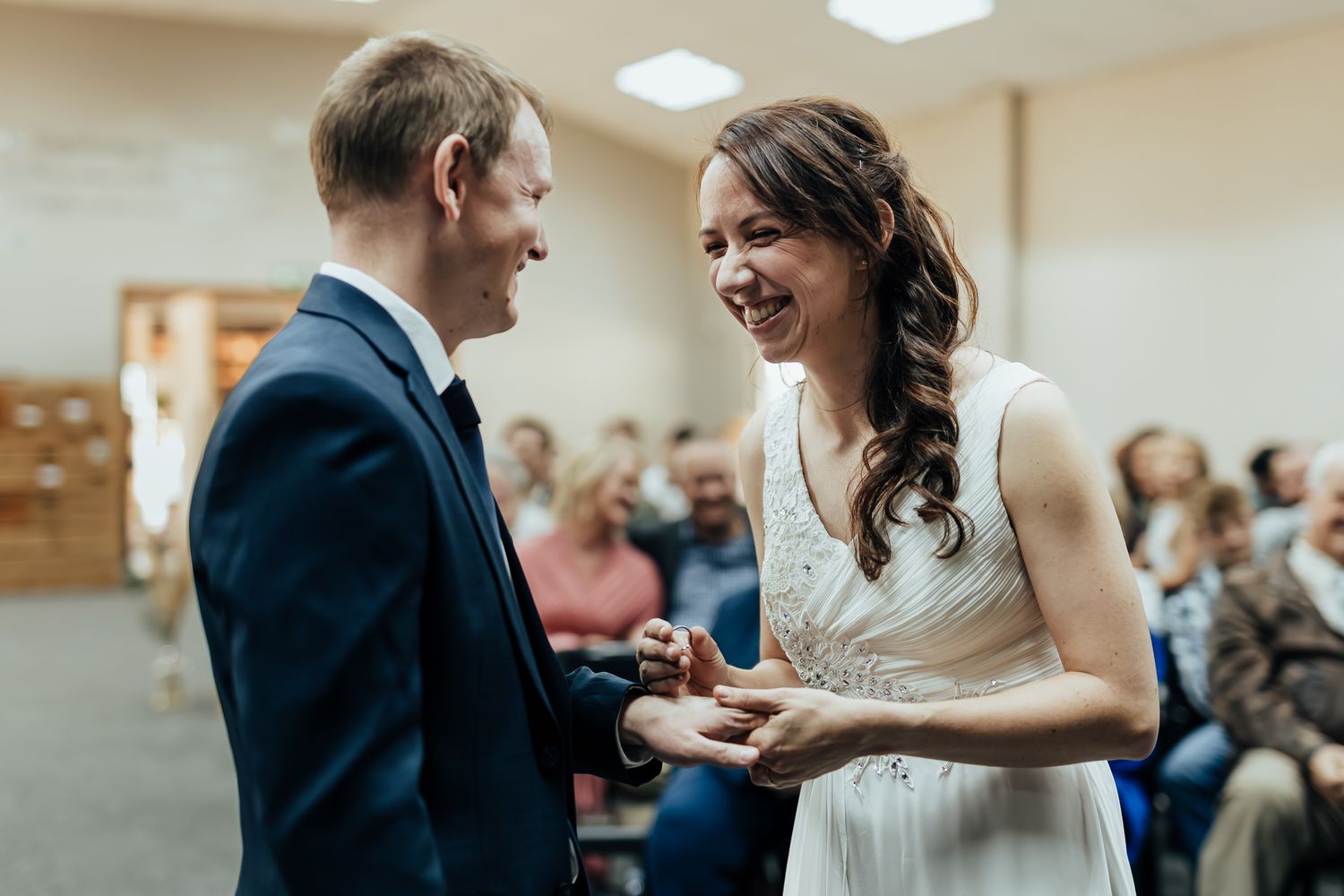 Couple sharing happy smiles during an indoor wedding ring ceremony.