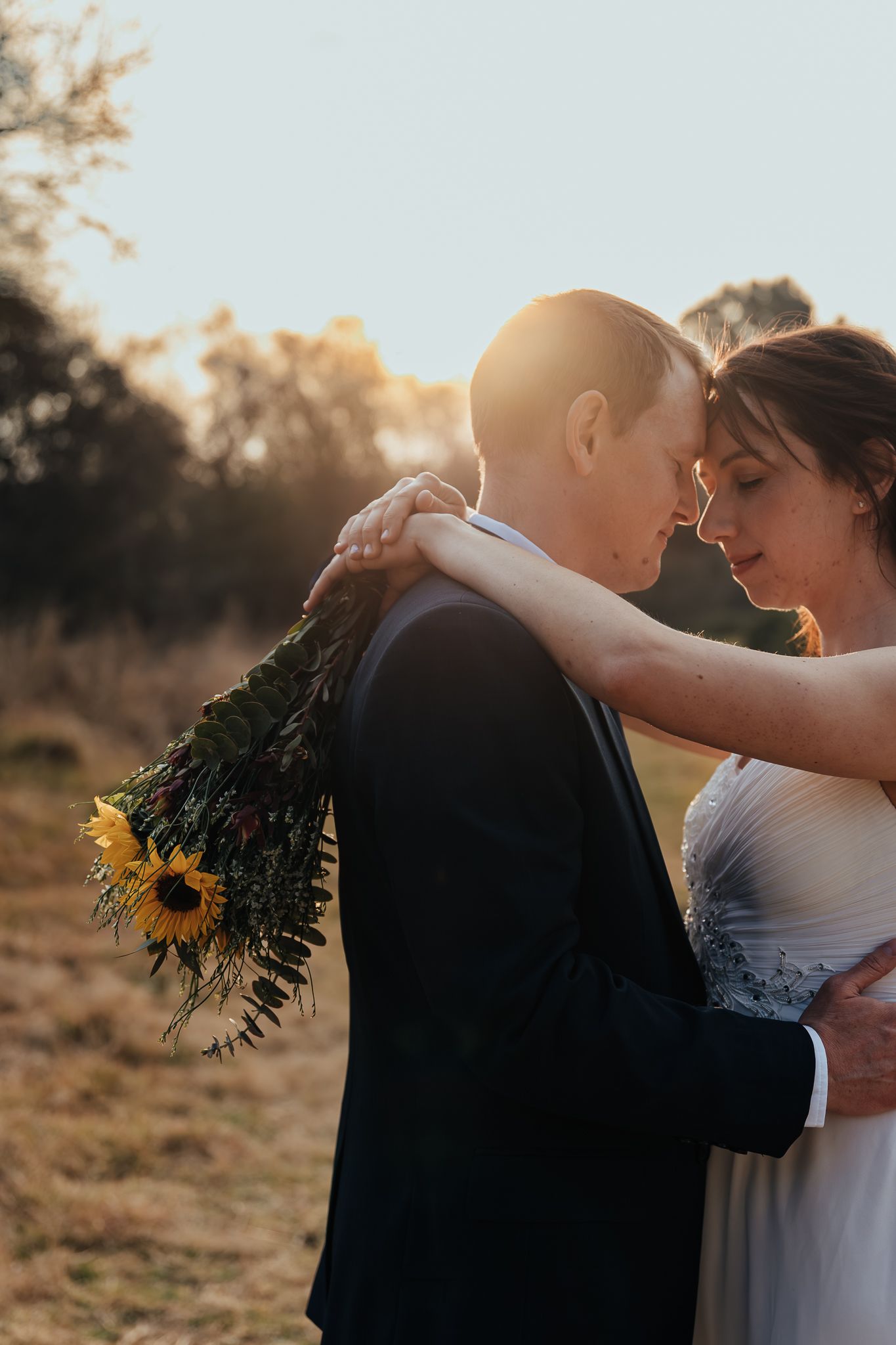 Silhouetted couple embracing at sunset with golden light and sunflowers in the background.