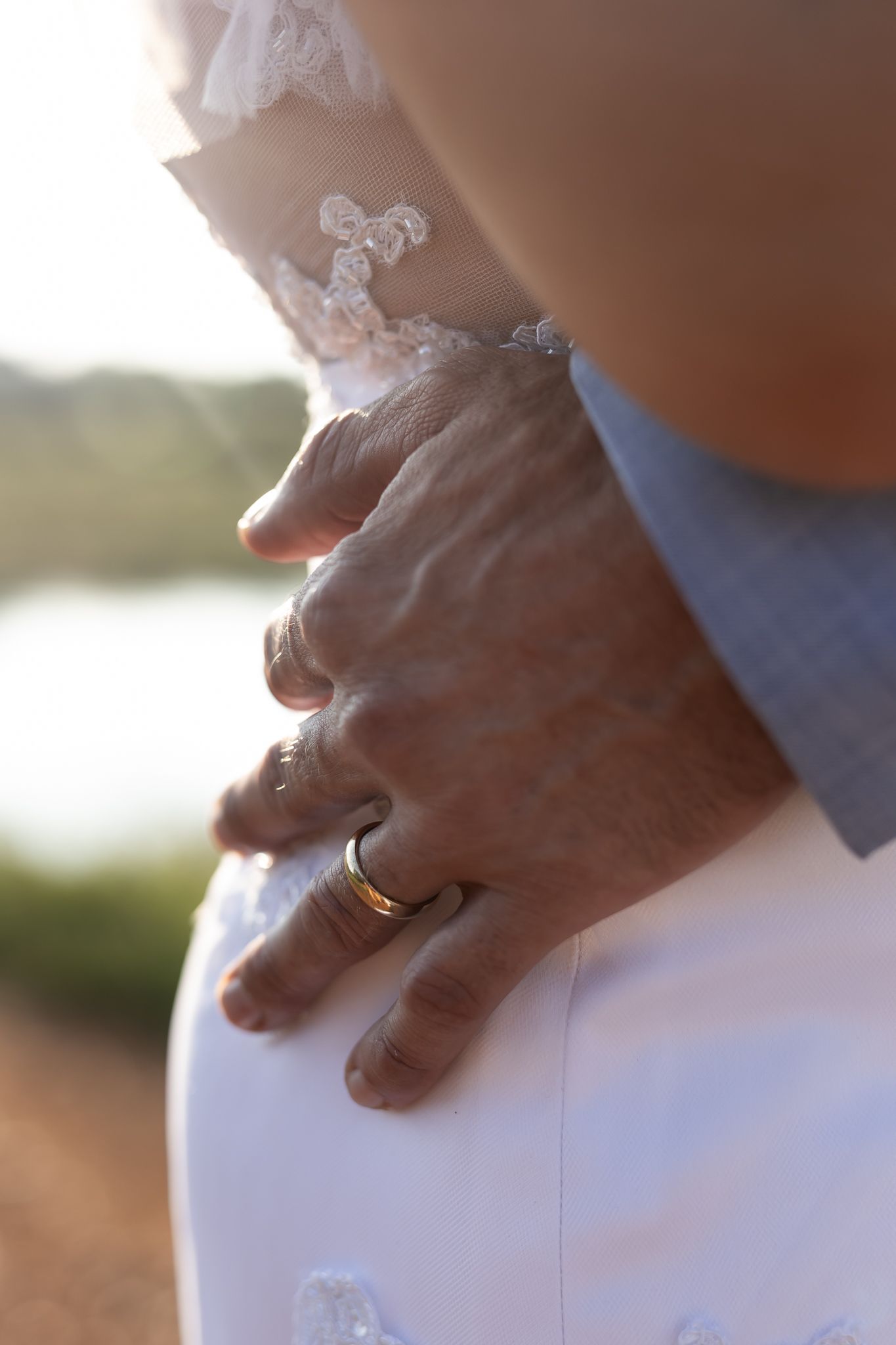 Close-up detail of wedding rings and lace dress during sunset portrait session.