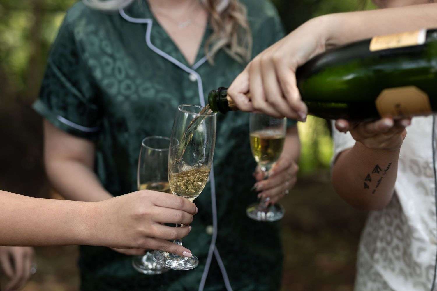 Hands pouring champagne into glasses at outdoor wedding celebration.