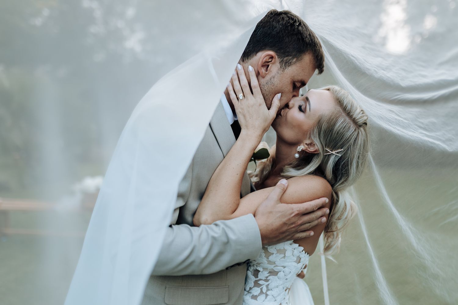 Ethereal wedding portrait with flowing veil and intimate embrace against misty background.