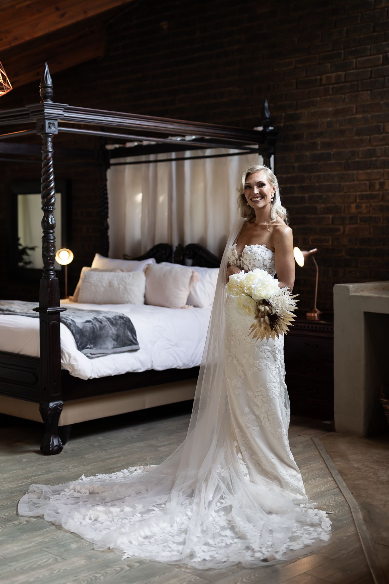 Full-length shot of bride in detailed lace wedding dress with cathedral train holding white bouquet.