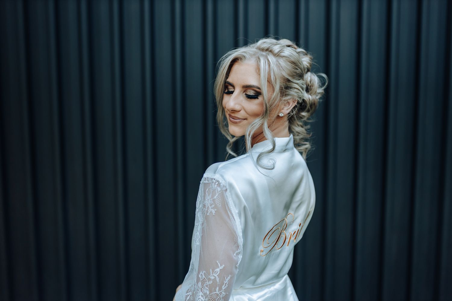 An elegant white satin robe with lace sleeves photographed against a dark curtain backdrop.