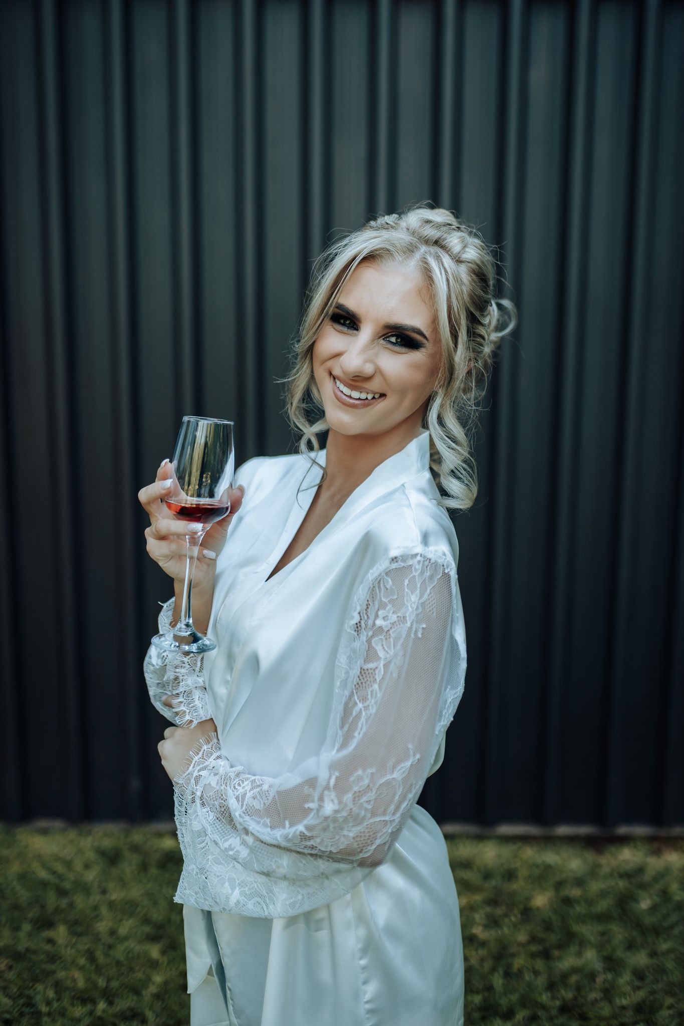 White satin robe with lace sleeves holding champagne glass against dark backdrop.