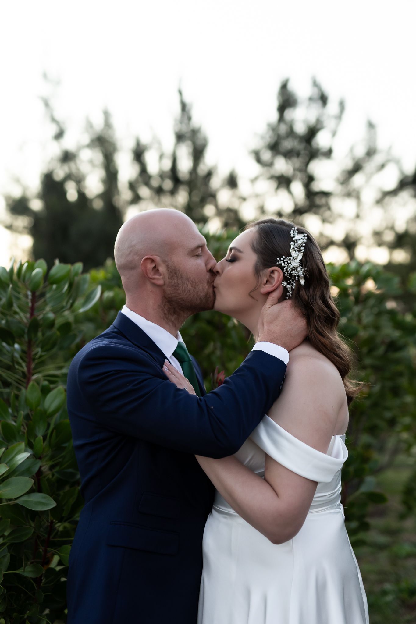 An intimate wedding kiss shared between newlyweds at dusk in a garden setting.