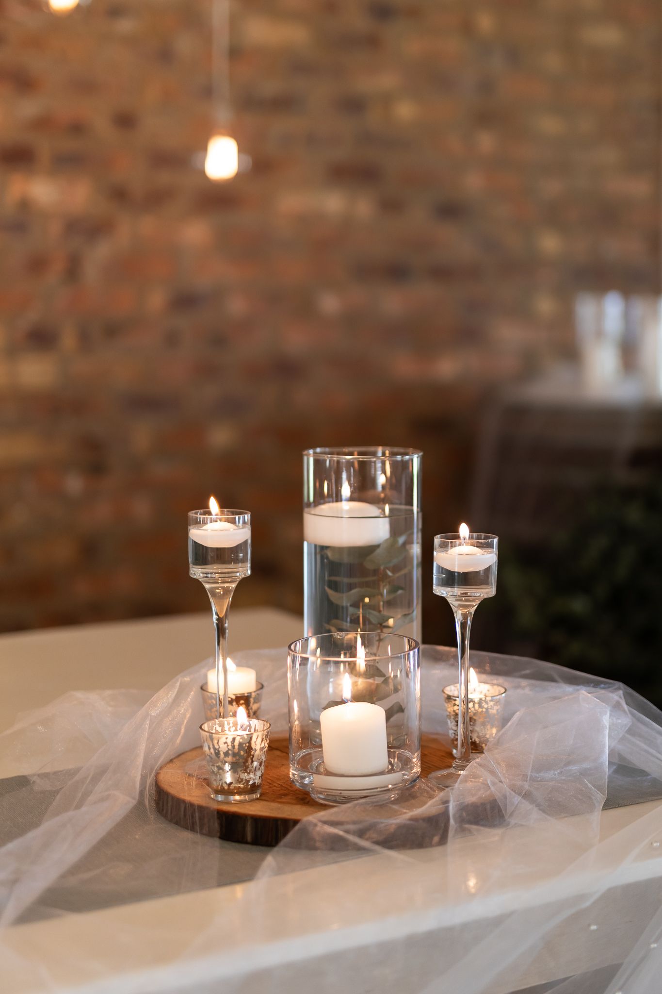 Elegant candle centerpiece with floating candles in glass holders on a wooden base draped with white tulle.